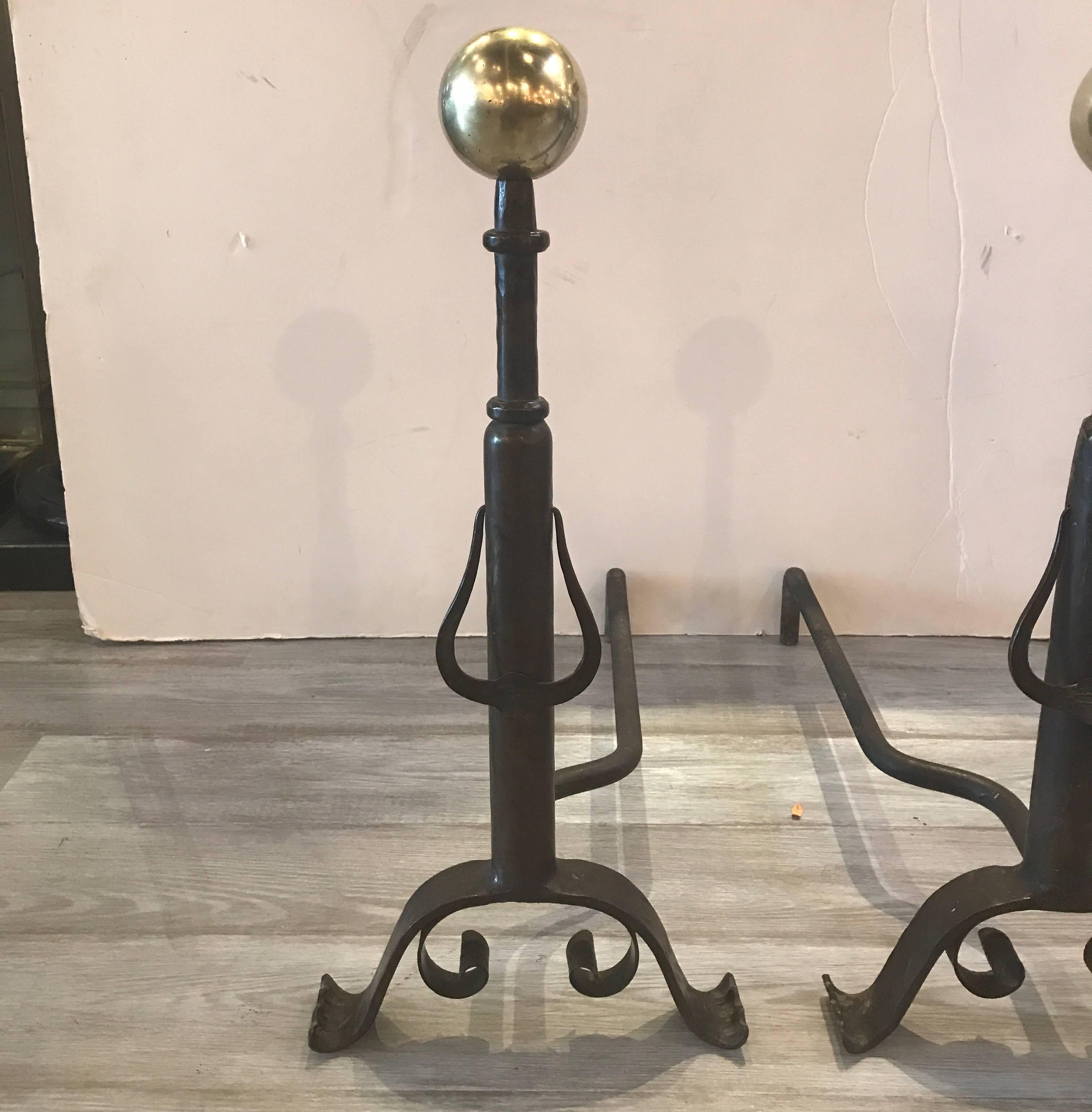 A Pair of late 19th century hand-hammered andirons. The polished cannon ball tops with patinated columns and iron back supports. The center column with a door knocker style pendant.