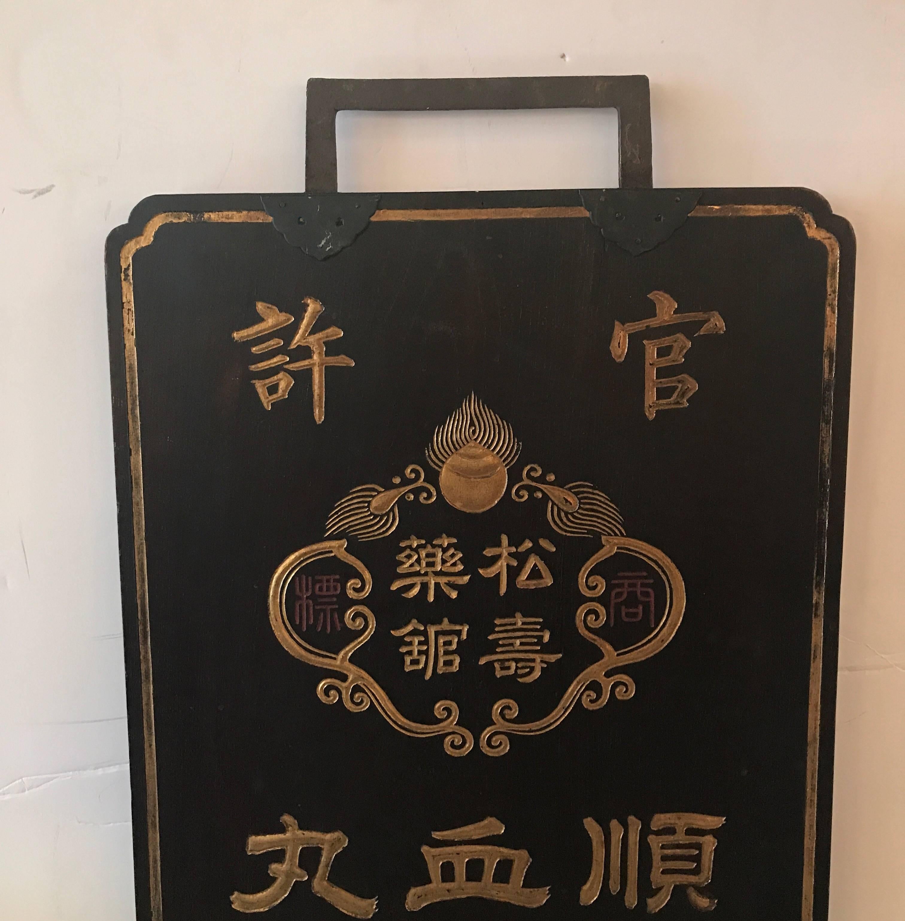 A hand-carved and painted double-sided Japanese wood trade sign. Solid wood panel with carved and gilt lettering with hand-forged iron mounts at the top.