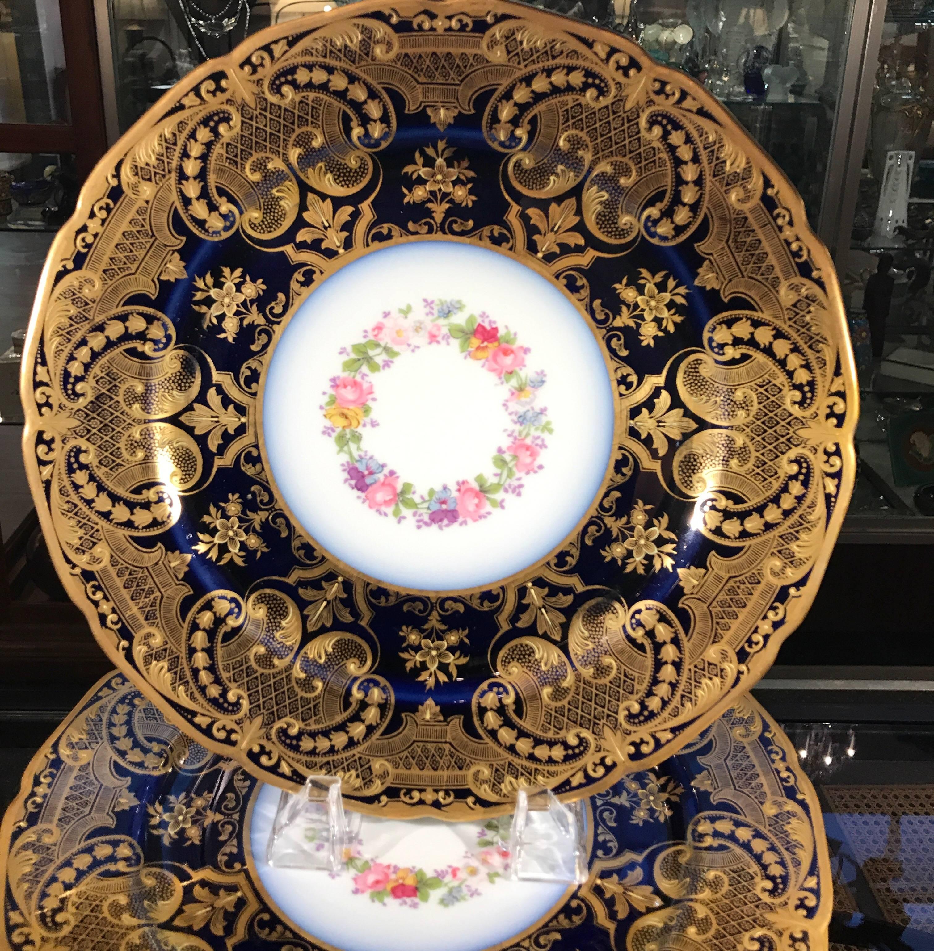 A set of 12 stunning elaborately gilt and cobalt bordered service plates. The opulent borders with raised gilt decoration with hand painted floral centers. Made by William Guerin Limoges France. This set is in excellent condition and were mostly