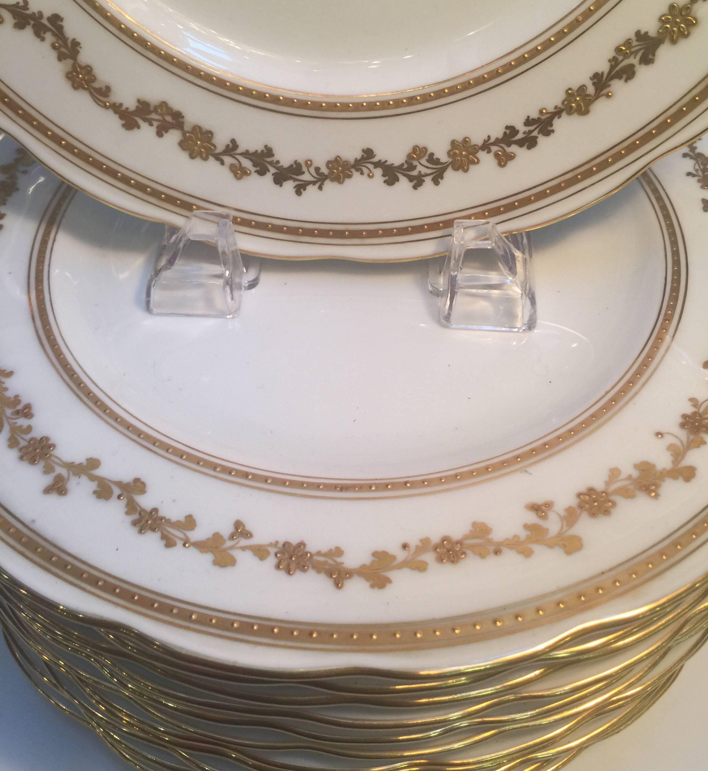 Elegant set of 12 raised gilt border dinner service plates with layered gold bands and floral band. The bone white background with scalloped edge.
