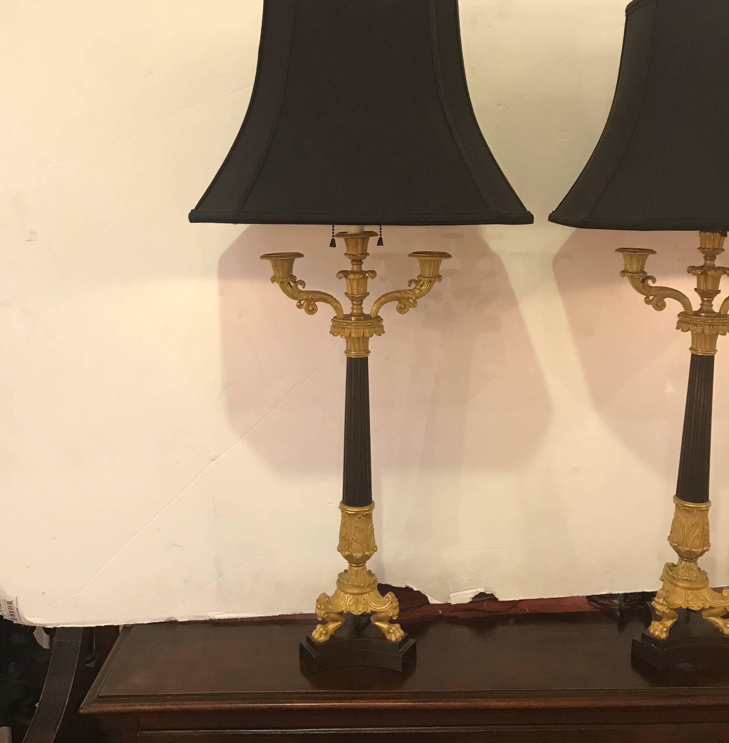 Three-arm bronze candelabra superbly cast and chased, each having three candle holders surmounted by gilt and patinated bronze columns with acanthus leaf decoration supported by a gilt tripod of lion's feet on a concave triform base with a gilt