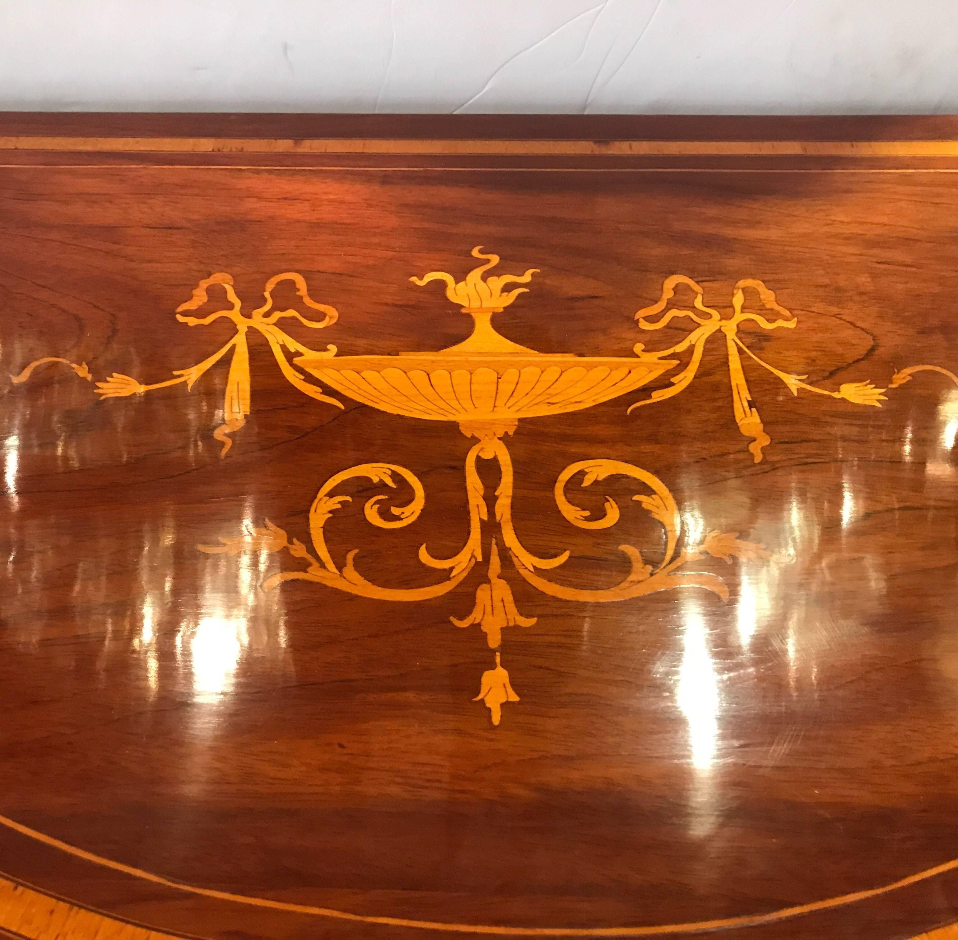 A highly inlaid pair of mahogany and satinwood inlay demilune console tables. The Classic Hepplewhite form with neoclassical inlay and bell flowers down the tapering legs. Elegant and hard to find pair.