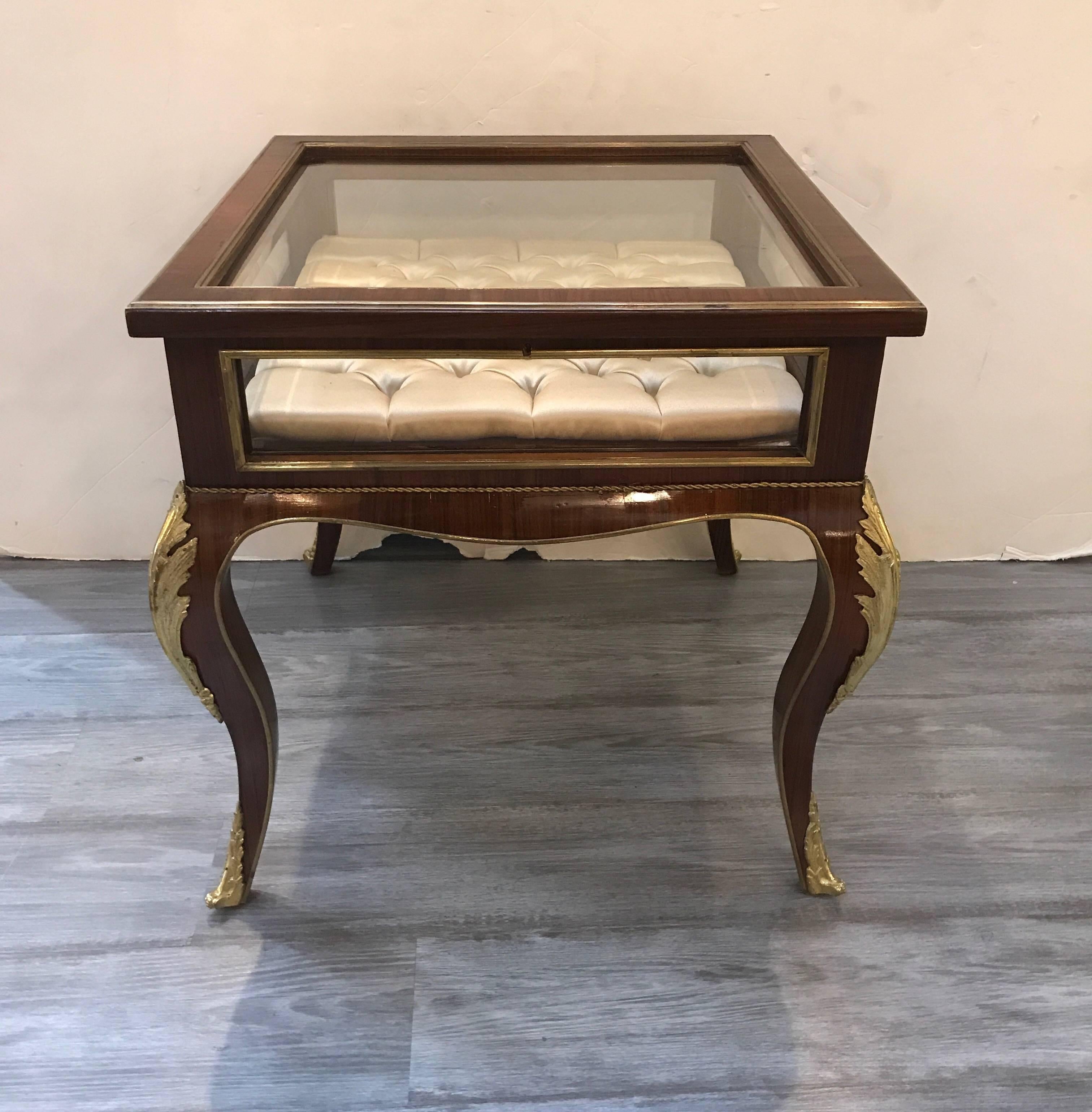 Opulent mahogany and gilt bronze-mounted lift top table vitrine. The louis XV style form with bronze trim and foliate mounts on the knees, the silk tufted interior with glass side panels and lift up door to display a treasured item or collection.