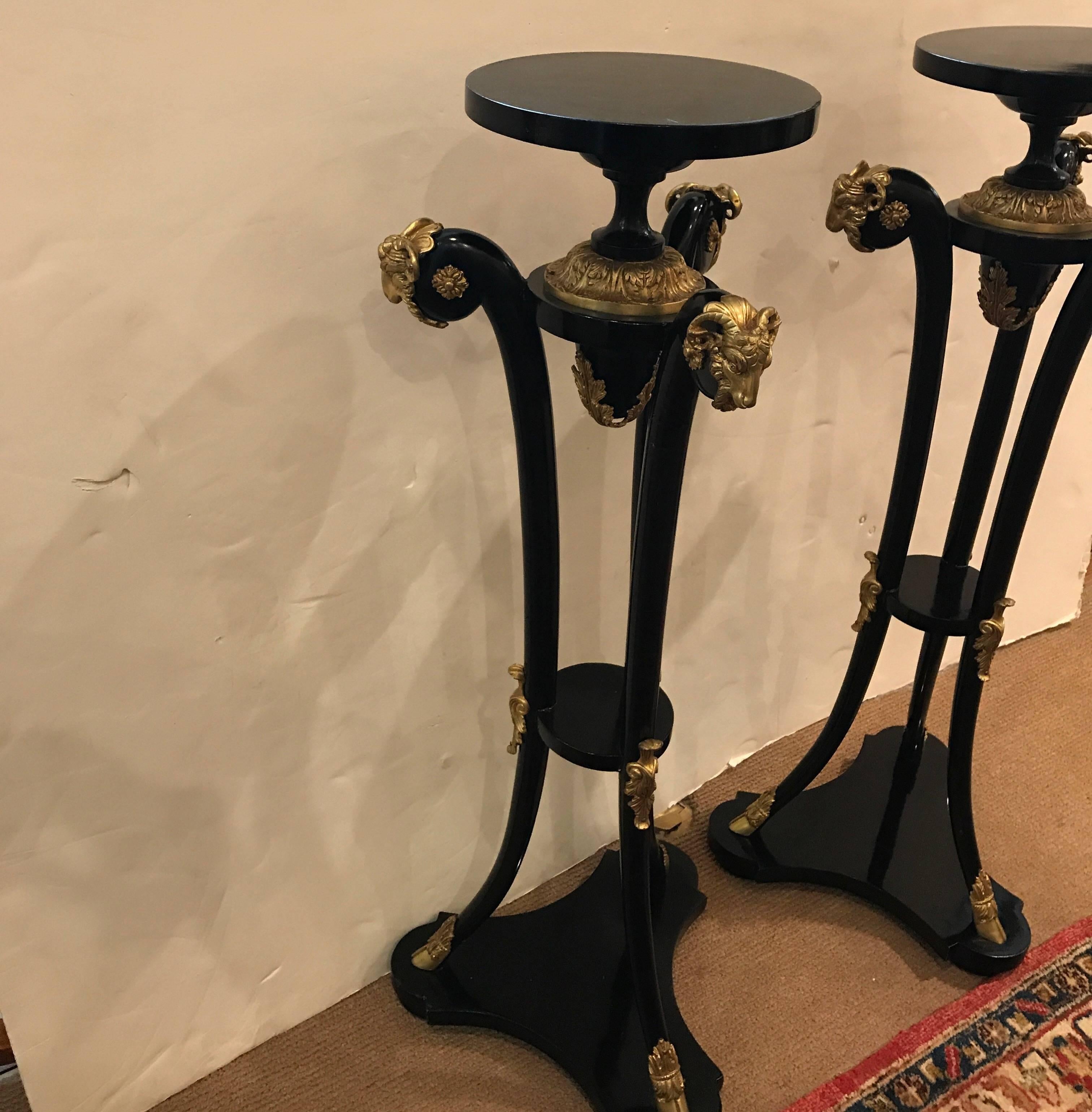 A very sophisticated pair of Empire style ebonized and ormolu pedestals. The round tops with centre column above the three flared legs with tripod base. The tops of the legs mounted with gilt bronze rams heads.