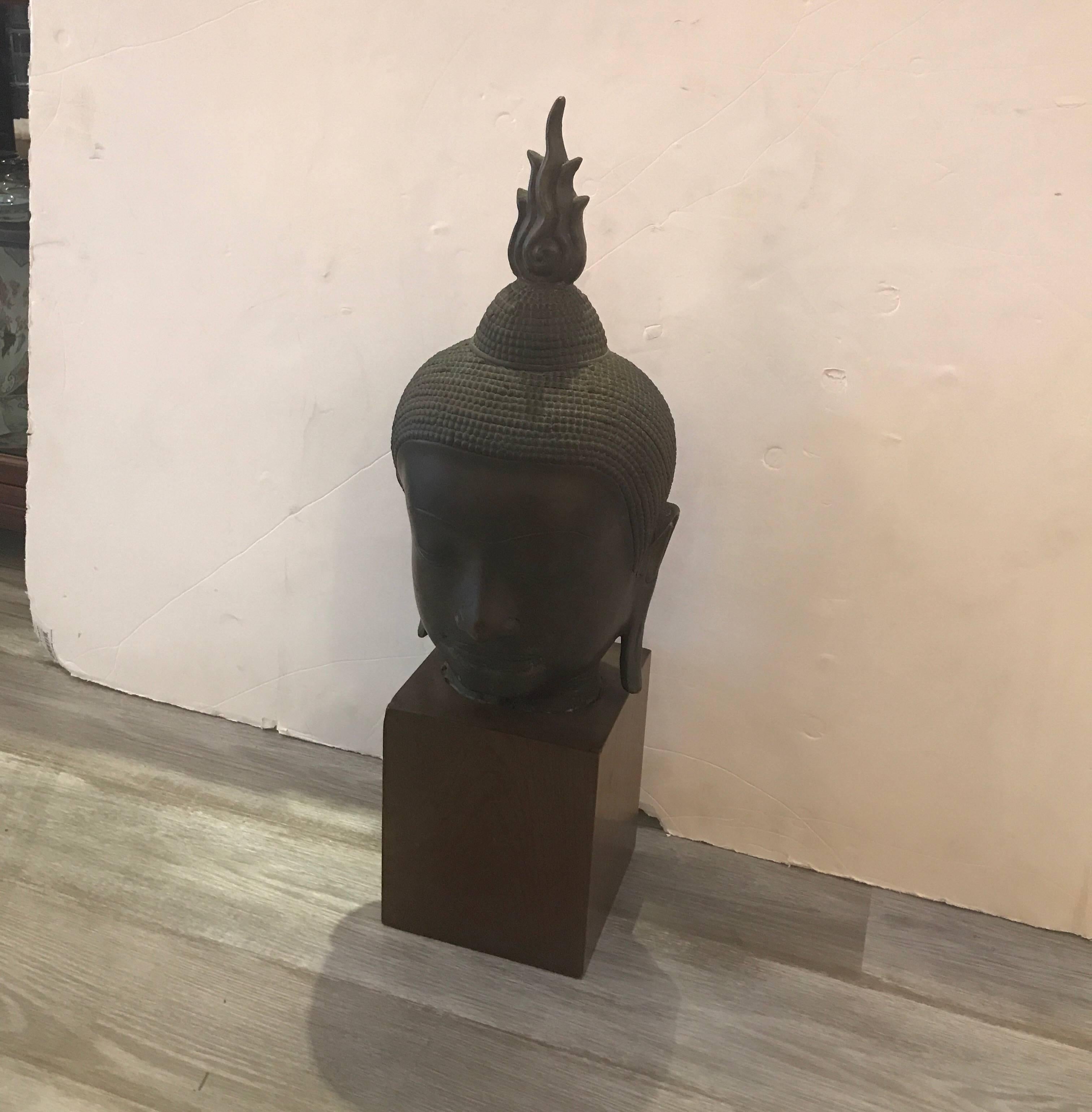 A cast bronze late 19th century Buddha head on solid walnut base. The antique bronze with original patination and aged finish on a later custom solid wood base. The base is 7 inches square. Overall height is 27.5 inches.
