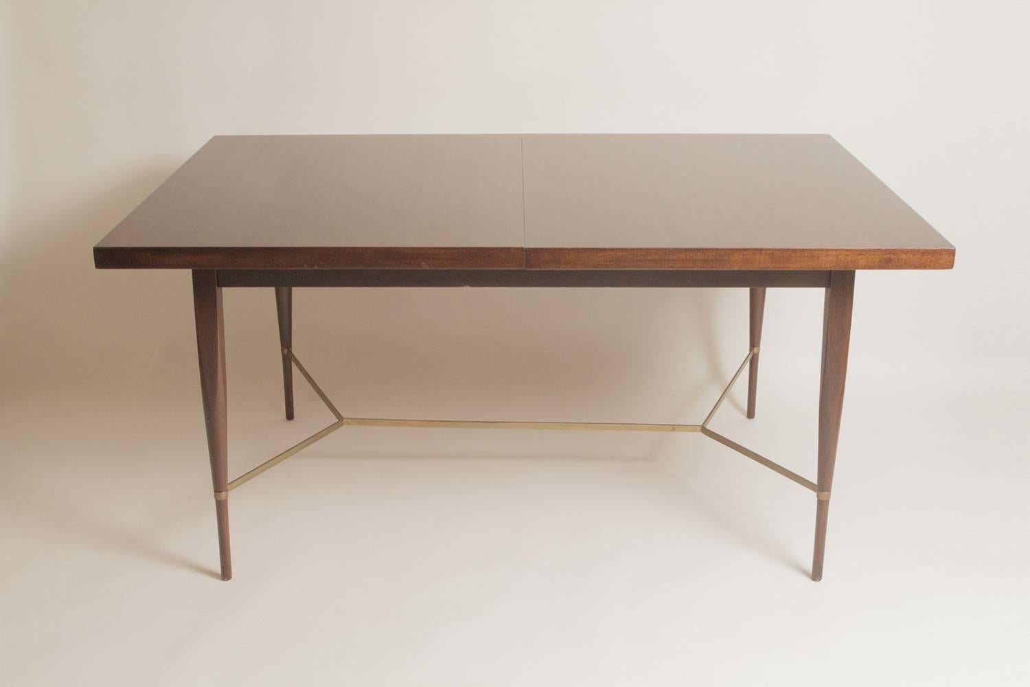 A mahogany and brass Paul McCobb dining table with brass 'y' stretcher.  60 inches long with 2 12 inch leaves for a full extension of 84.  Designed by Paul McCobb for the Calvin/Irwin Collection.  The chair seats have been recovered and the table