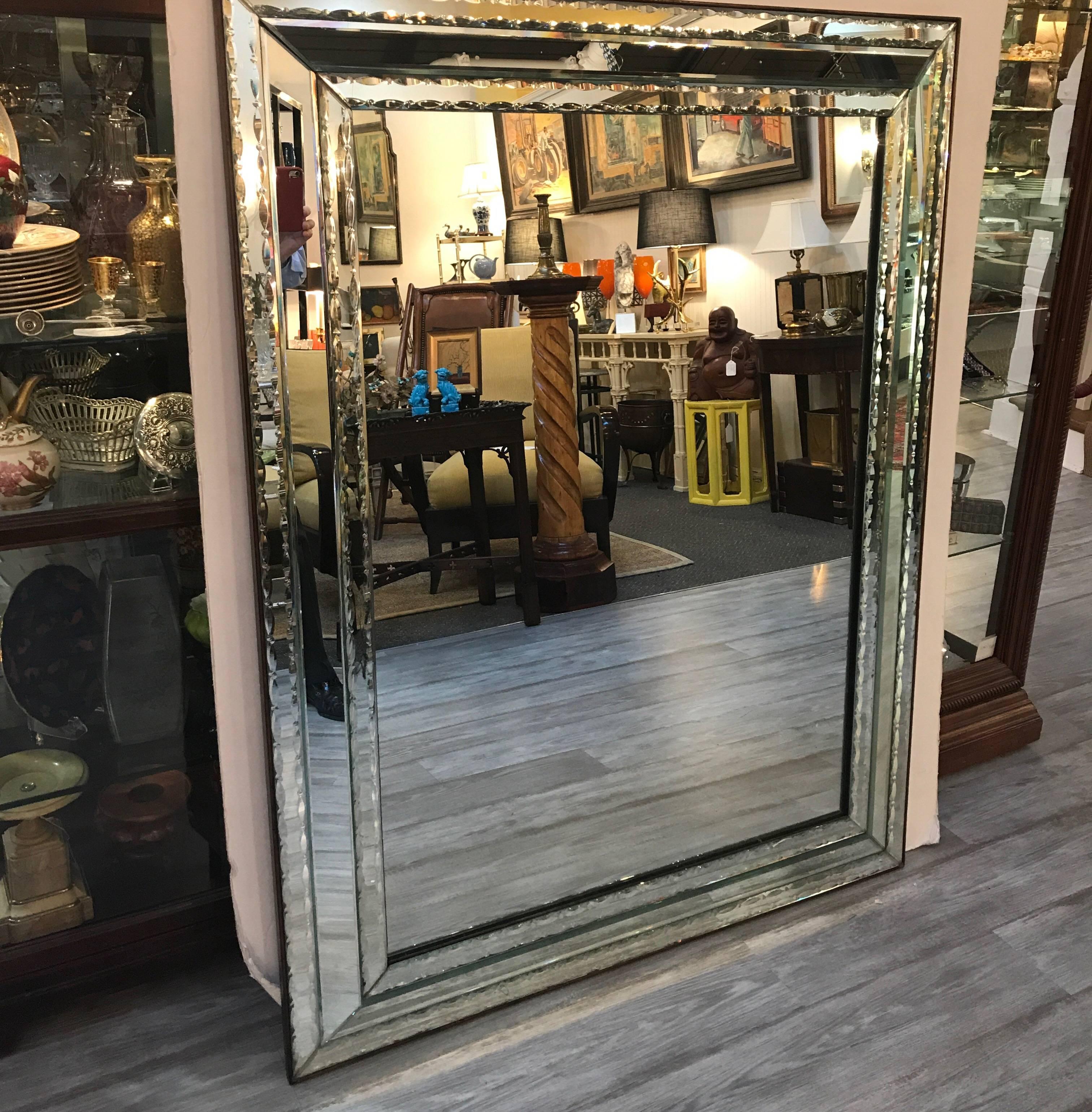 A large and elegant antique Venetian mirror made in Italy in the 1920s. The mirrored frame with cut scallop edges with a mahogany trim and back. This mirror is unique as it is more tailored and has an Art Deco influence.