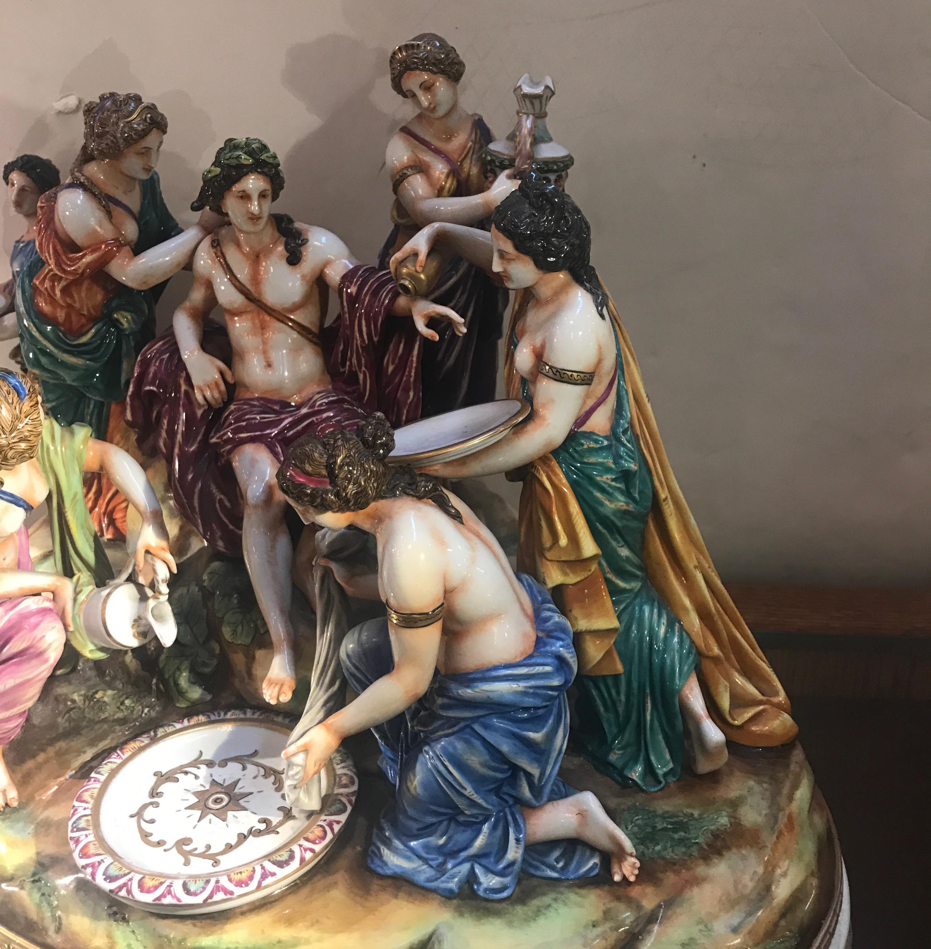 Impressive and large multi figurative porcelain sculpture of a Greek man surrounded by six Greek maidens on a large oval base. Vibrant and highly detailed with gilt highlights. Marked on the lower back, blue under-glaze with the capodimonte mark.