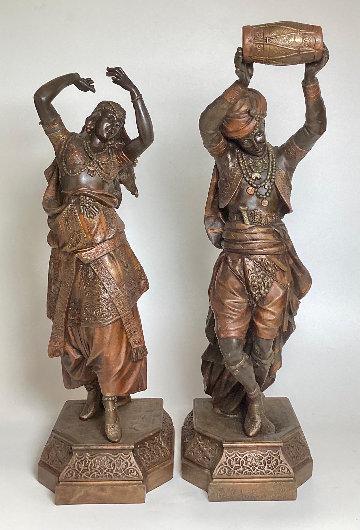 A Pair of Orientalist style Figures of a musician and dance, cold painted over white metal, with an old repair ot the base of the male.  