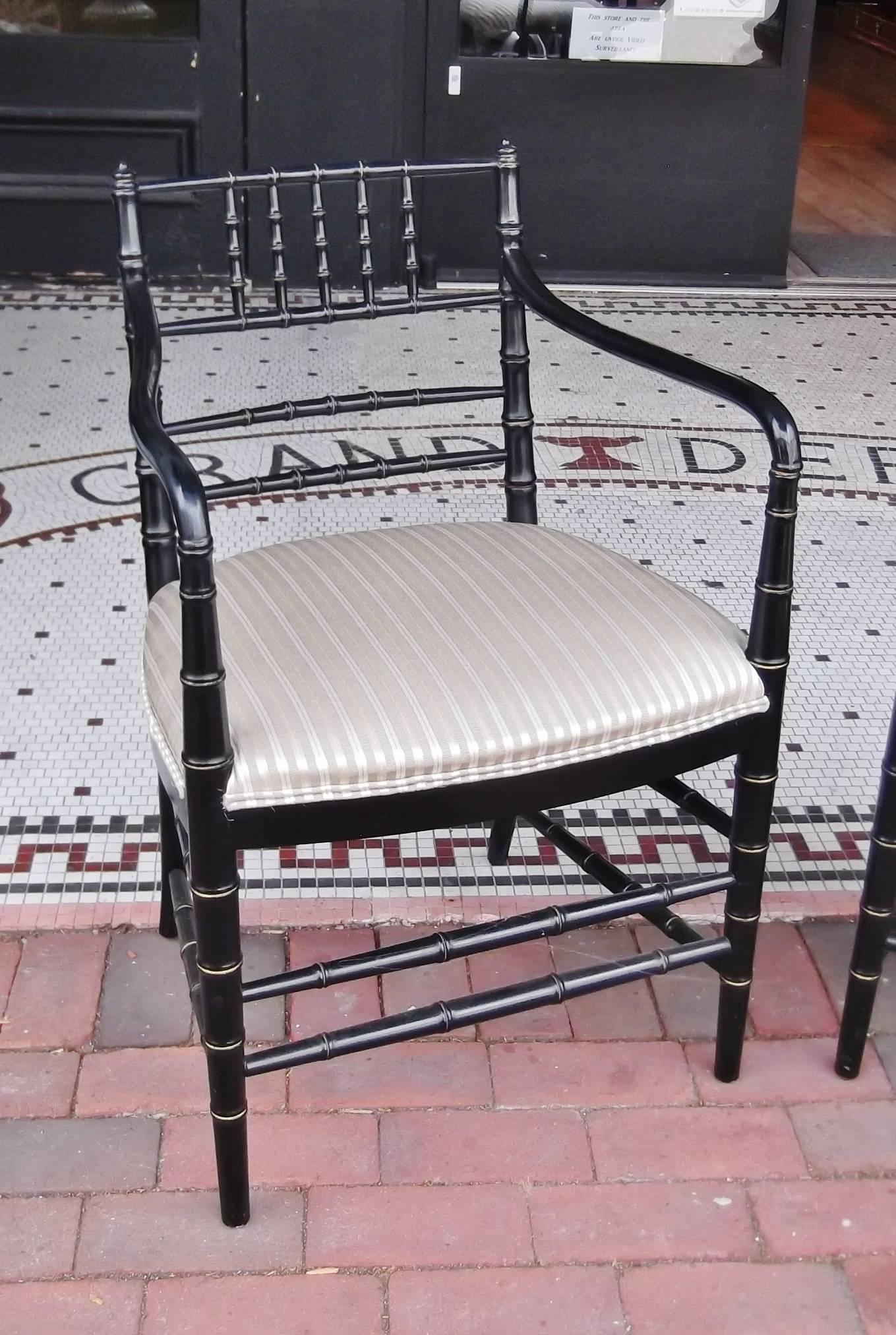 A pair of ebonized wood accent armchairs with newly upholstered seats. Simple chic Regency styling, the frames are a carved bamboo style with a sinuous arm. The seats are hand tied spring coils, giving a high quality seat support. There are subtle