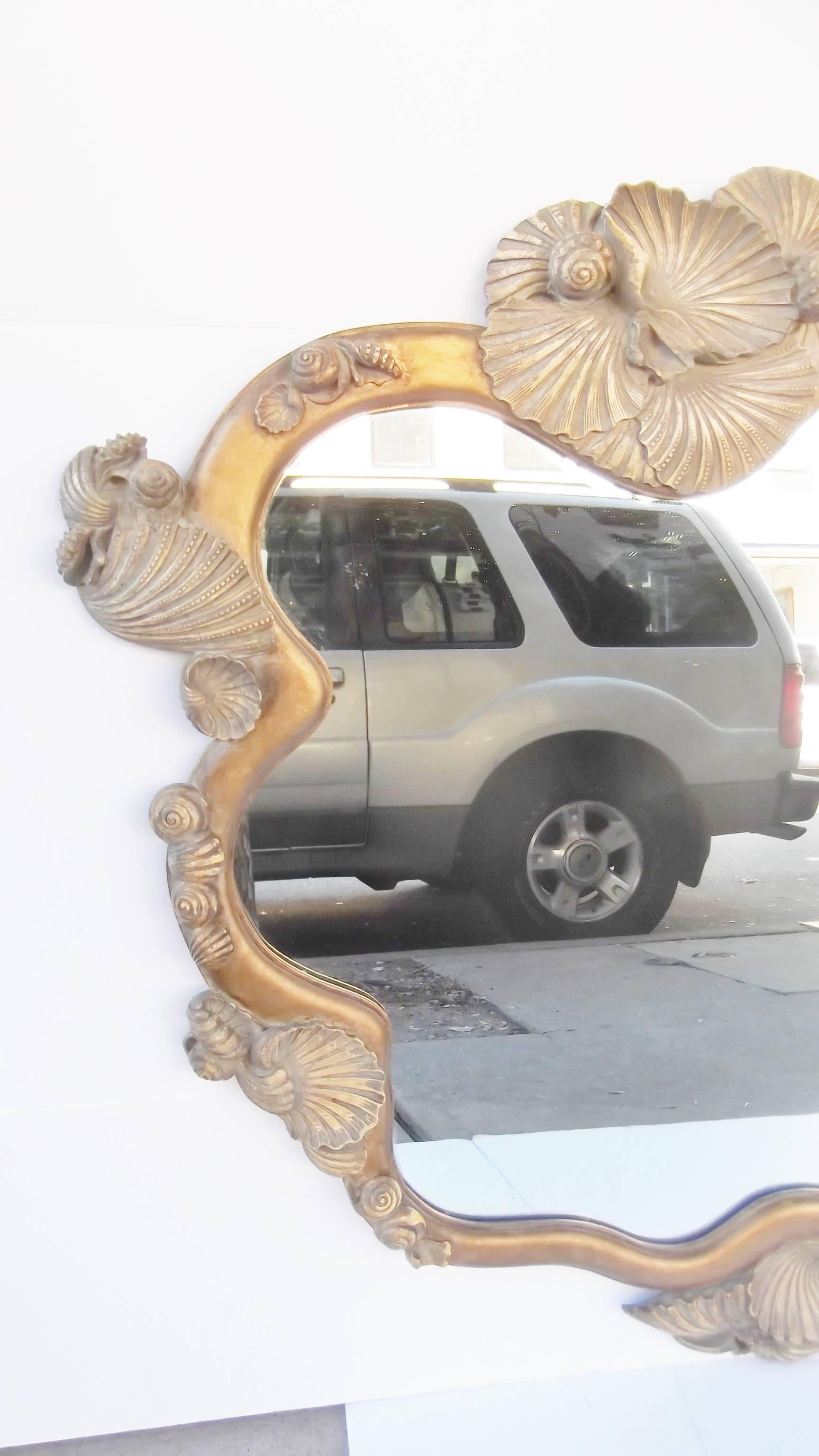 A very interesting shell design mirror, perfect for a beach home .The frame is wood and plaster with a dull matte finish to the frame.  The shapely shells are more of an Ivory Beige.  Large size with a free form overall shape.  The back is a secure
