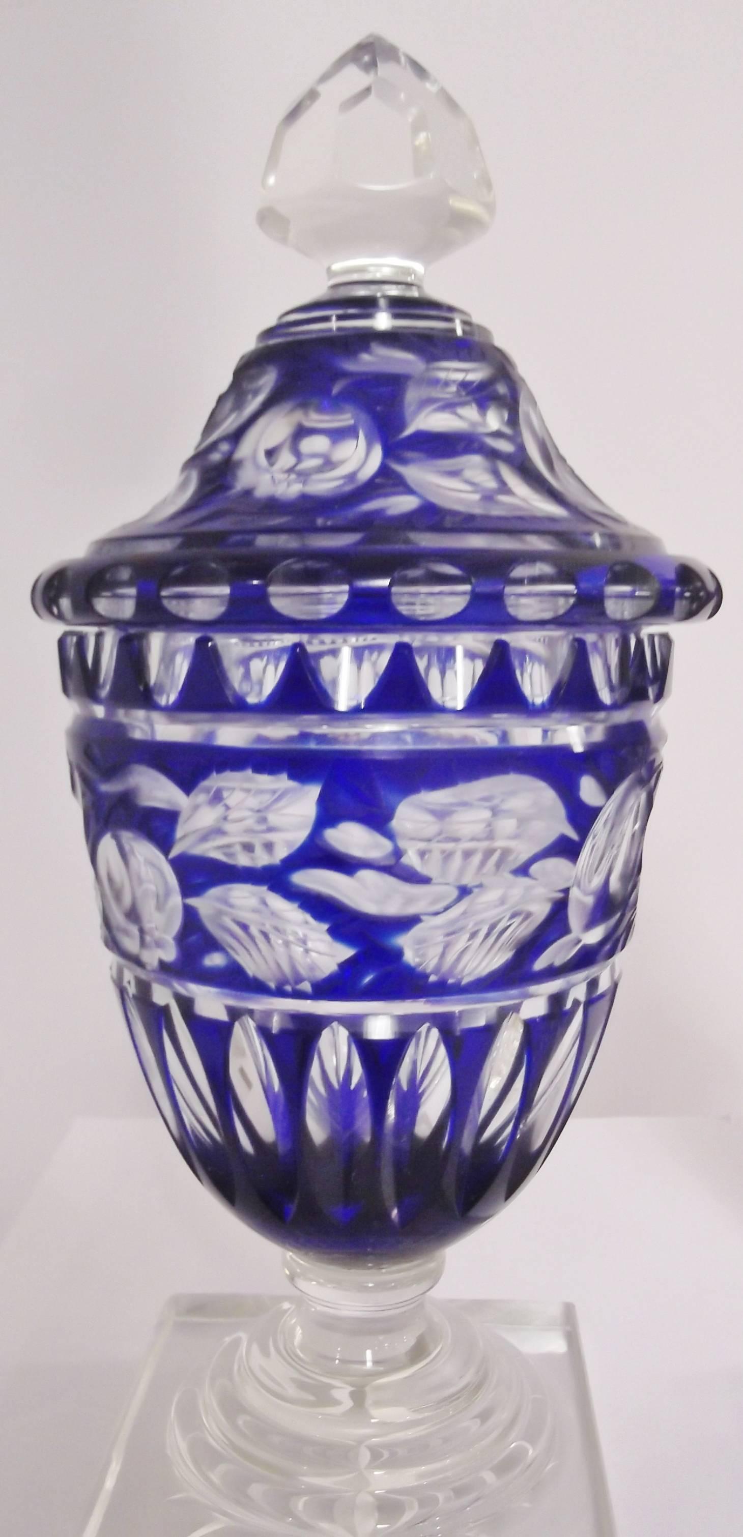 An exceptional pair of English cobalt cut to clear glass urns.  Faceted finals on the lids with sculpted fruit designs all over. The bodies of the urns have deep vertical cuts all resting on pedestal plinth bases.  Expert quality cutting attributed
