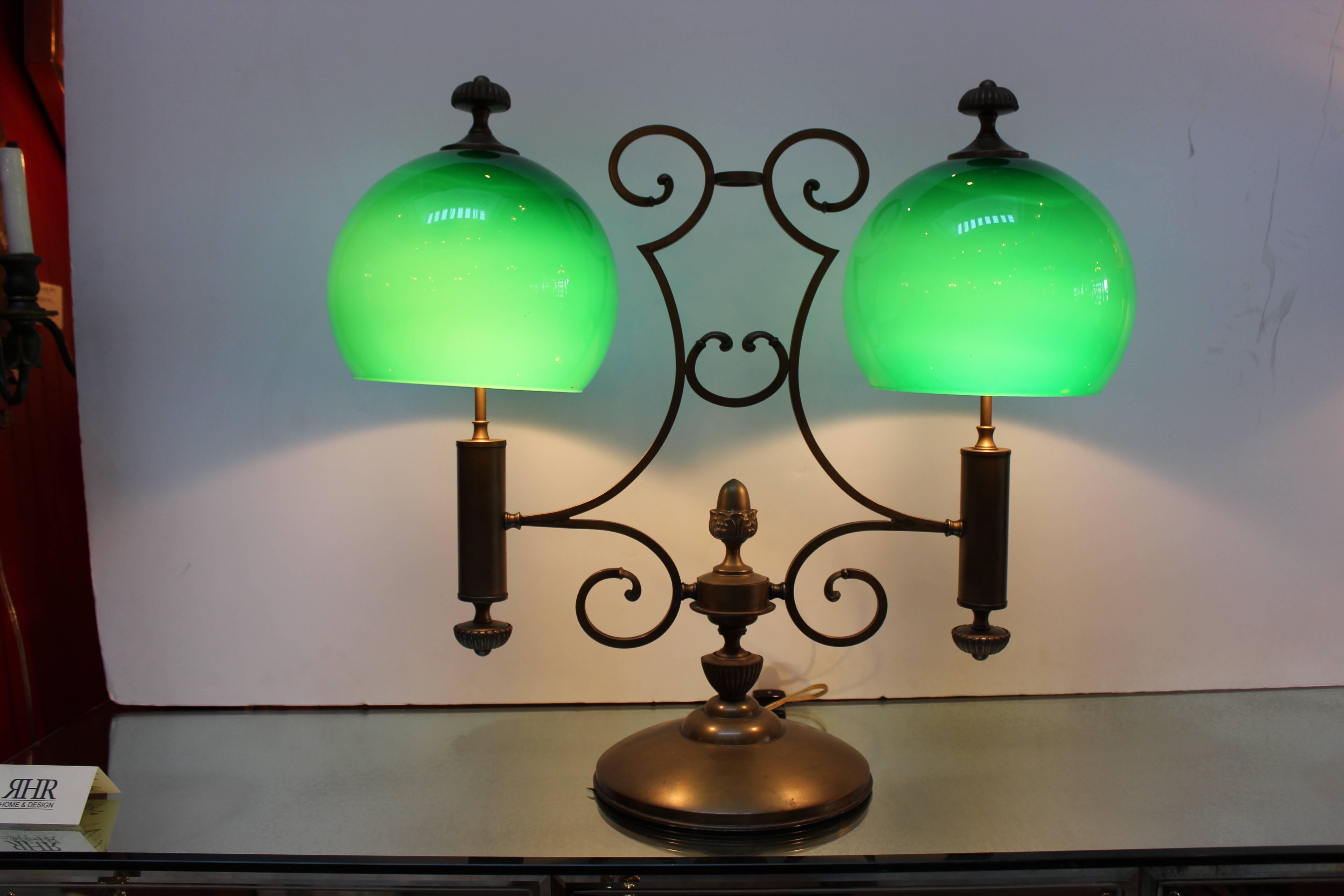 Very stylish double light library lamp. Two emerald green glass shade lined with white glass over the scrolled brass body resting on a pedestal base, early 20th century.