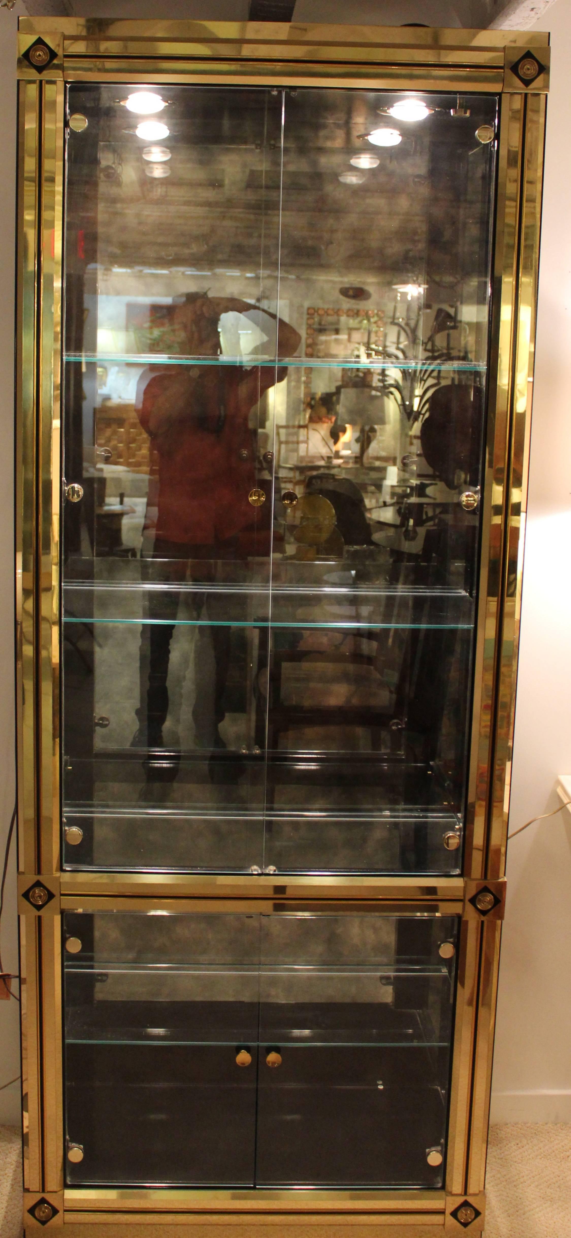 Glamorous brass clad display cabinet made by Mastercraft. The corners have black geometric trim giving this vitrine an empire revival feel. The shelves are glass with an antiqued mirrored back. The cabinet retains its original makers label. The