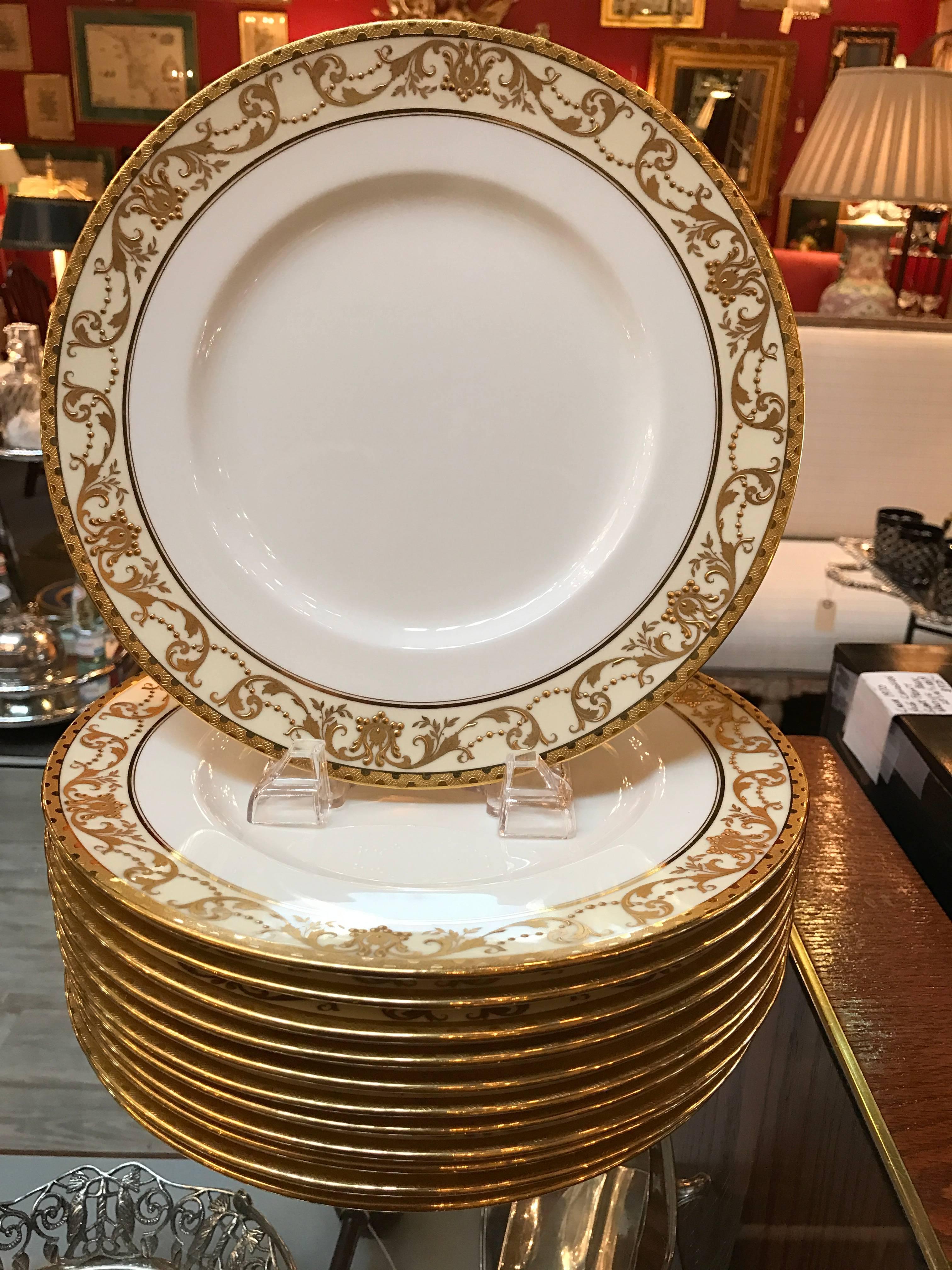 Elegant set of 12 raised gilt service plates made by Minton. The delicate borders with a raised gilt pattern. The background color is a light vanilla with a white porcelain center, the mark on the bottoms represents a year of 1905, all in wonderful