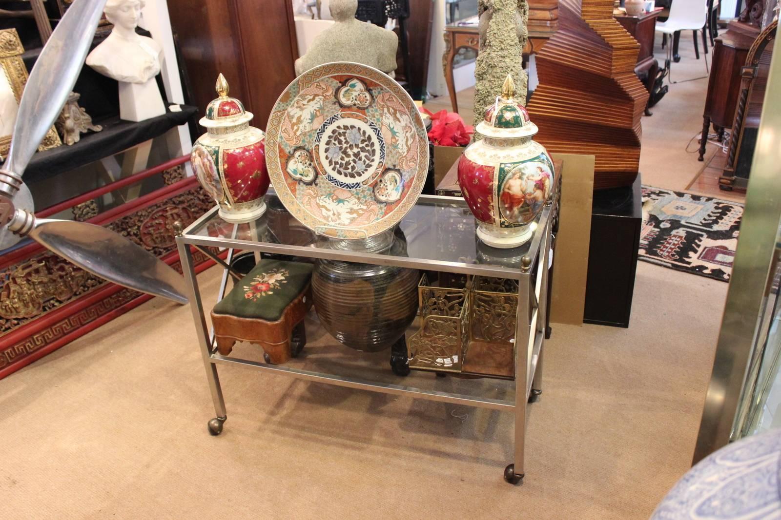 High style steel and glass Hollywood Regency beverage cart. The simplistic lines with brass finial tops and neoclassical influenced X-support on the sides. The carts is supported by four castors.
