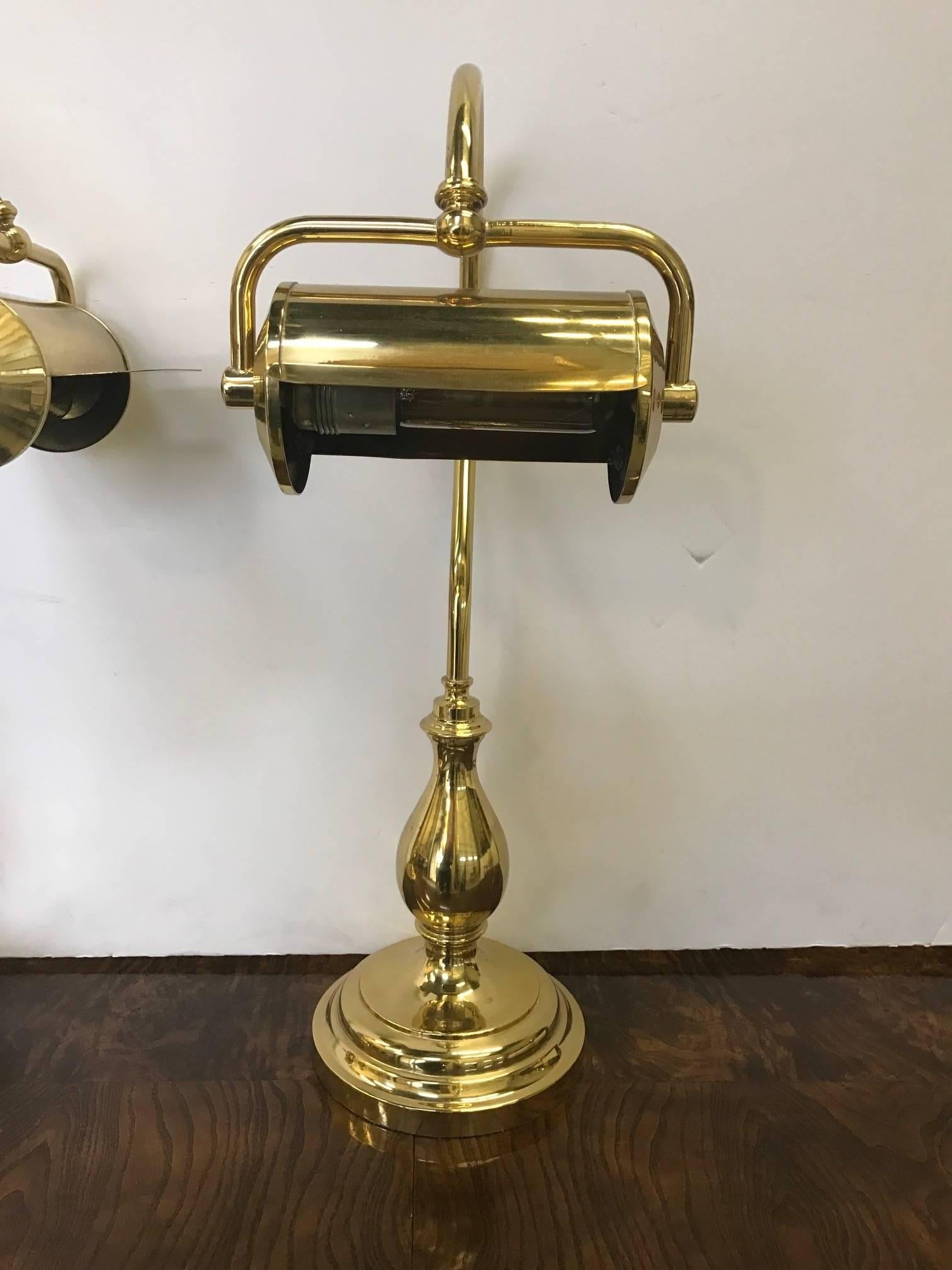 A handsome pair of brass adjustable goose neck library lamps attributed to Chapman. The front lamp with adjustable shade attached to a curved goose neck arm supported by a bulbous round plinth base. Each lamp has a switch located on the lamp cord,