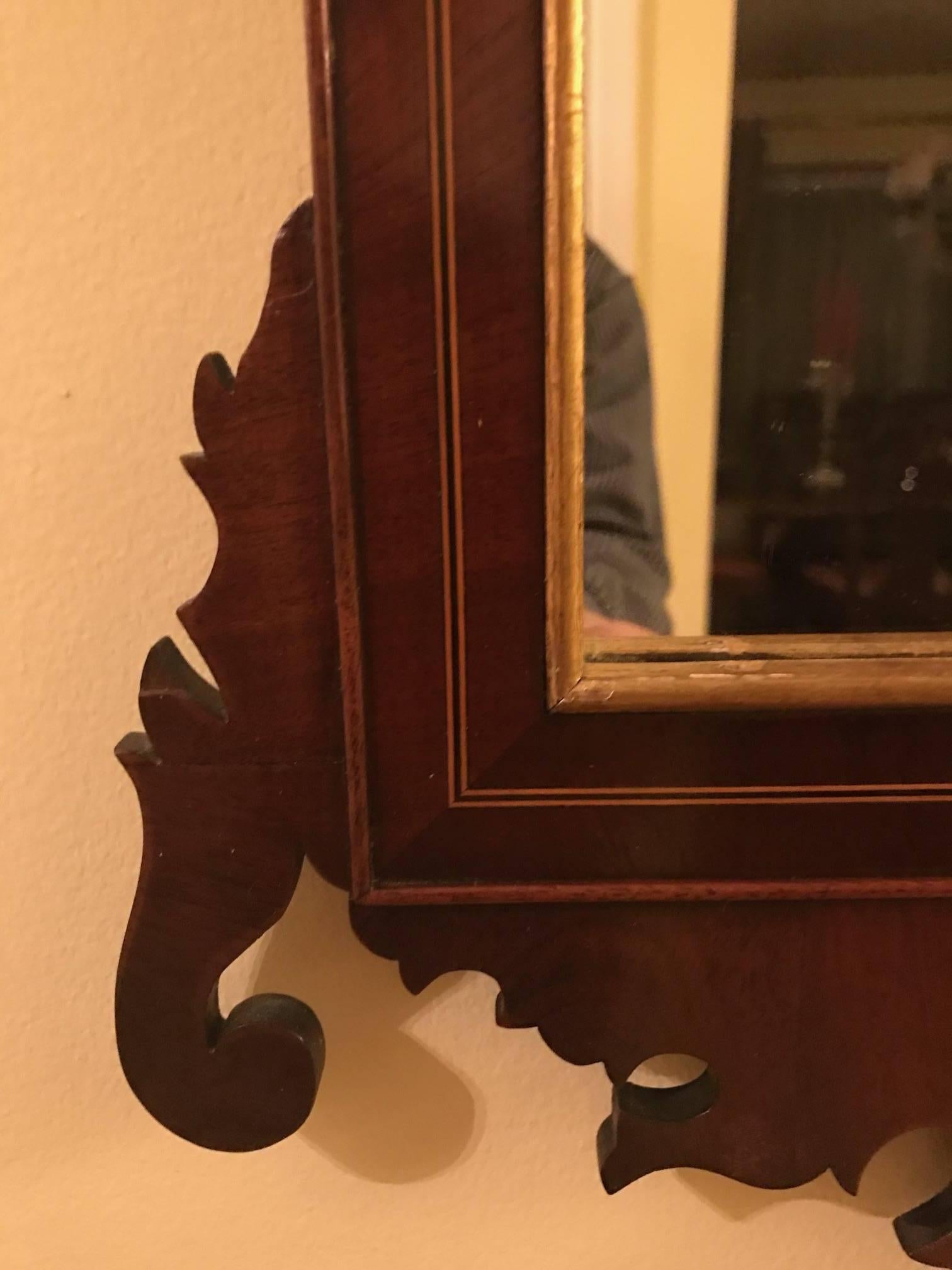 Elégant miroir en acajou de style Chippendale du 19e siècle. Le fronton en col de cygne doré est orné d'une rosette et d'un motif d'urne, flanqué de délicates vignes dorées avec des branches. Le miroir est souligné par une incrustation de lignes de