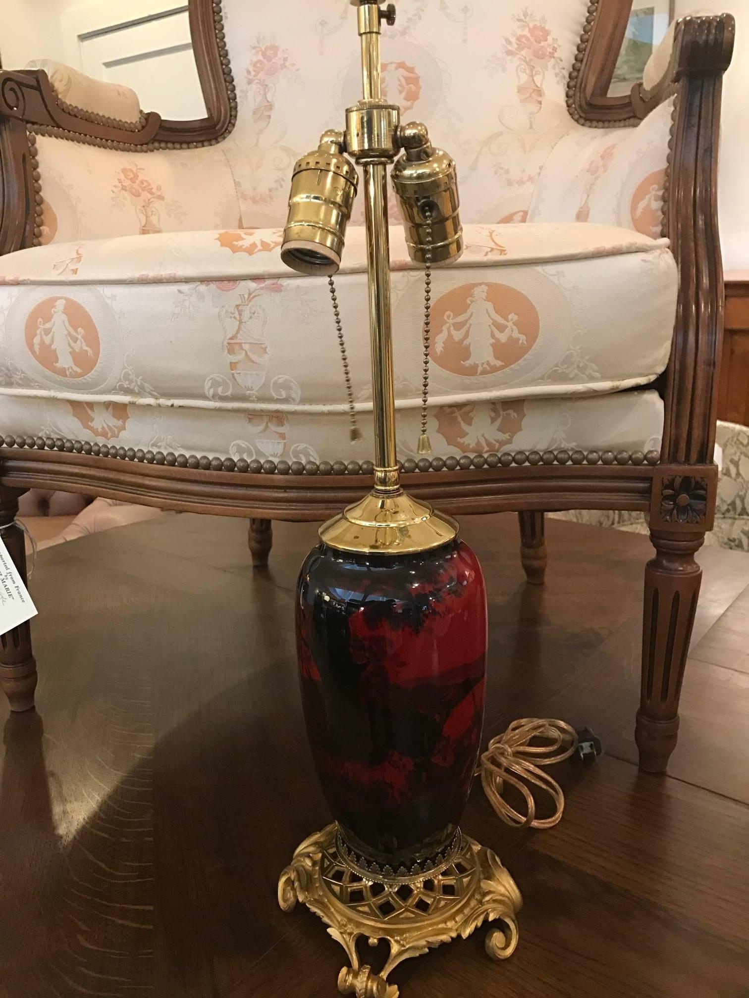 Exceptional pair of English flambe glazed ormolu-mounted lamps. Made by Royal Doulton in the early 20th century, these rich red glazed lamps are hand-painted by Charles Noke of the Royal Doulton porcelain and pottery makes. The bases are elegantly