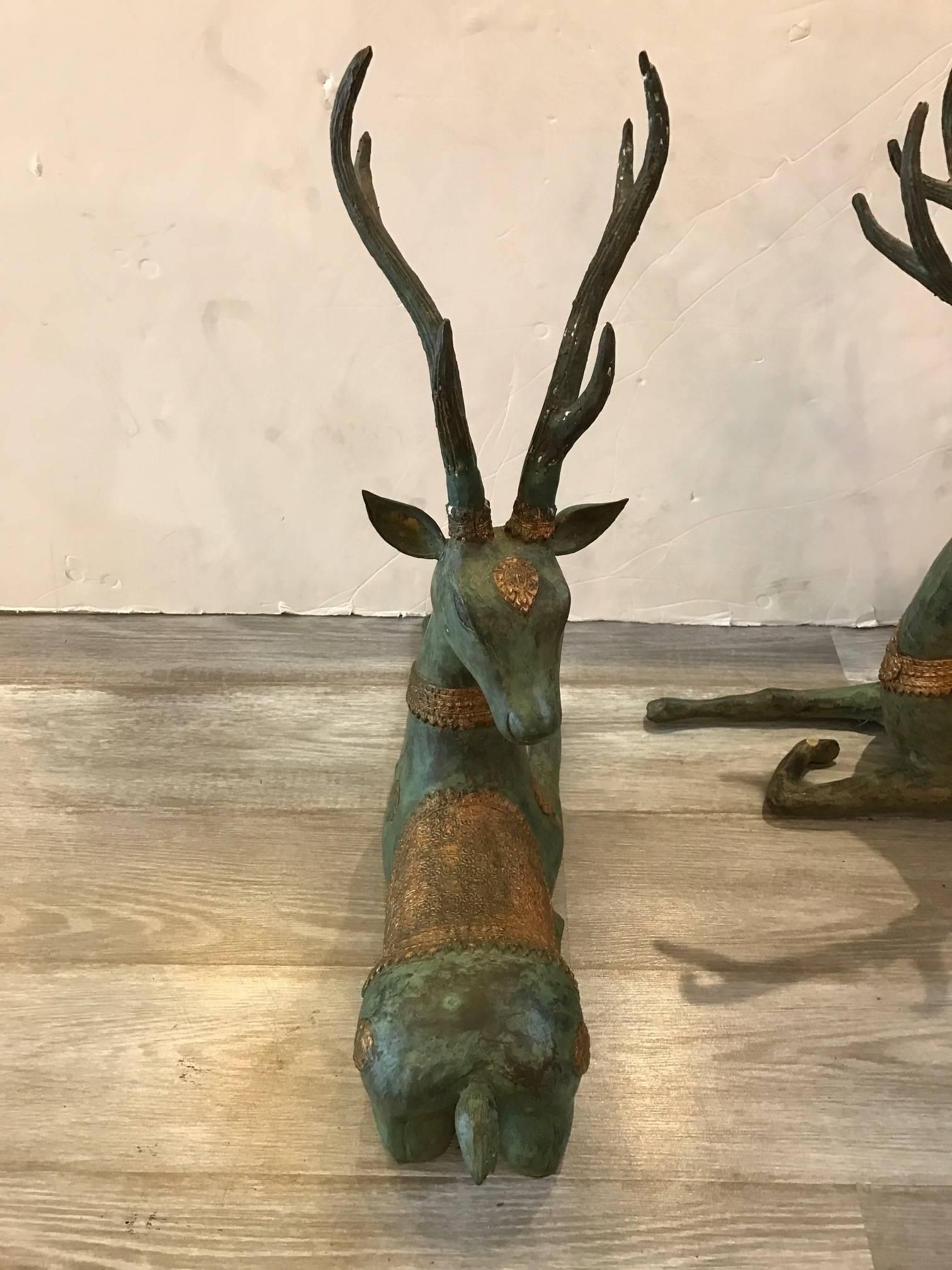A pair of antique style bronze deer statues from the early 20th century. The original green oxidized and patinated finish are highlighted with gilt decoration. Original mirror image pair. 