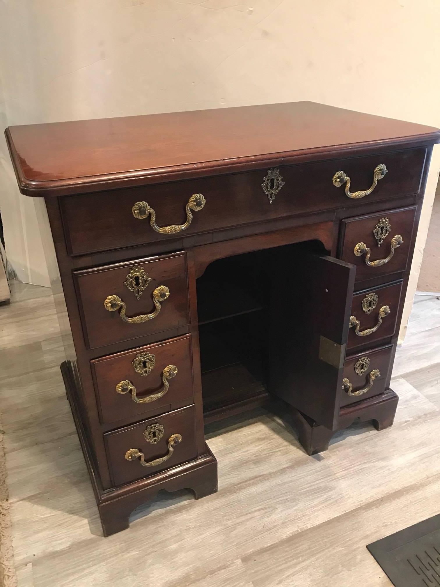George III Mahogany knee hole desk, circa 1780-1800. The bull nose edge top over a central drawer above a cupboard door flanked by a series of three drawers. The thumb molded drawers retain cast fire-gilt brasses,  the piece rests on bracket