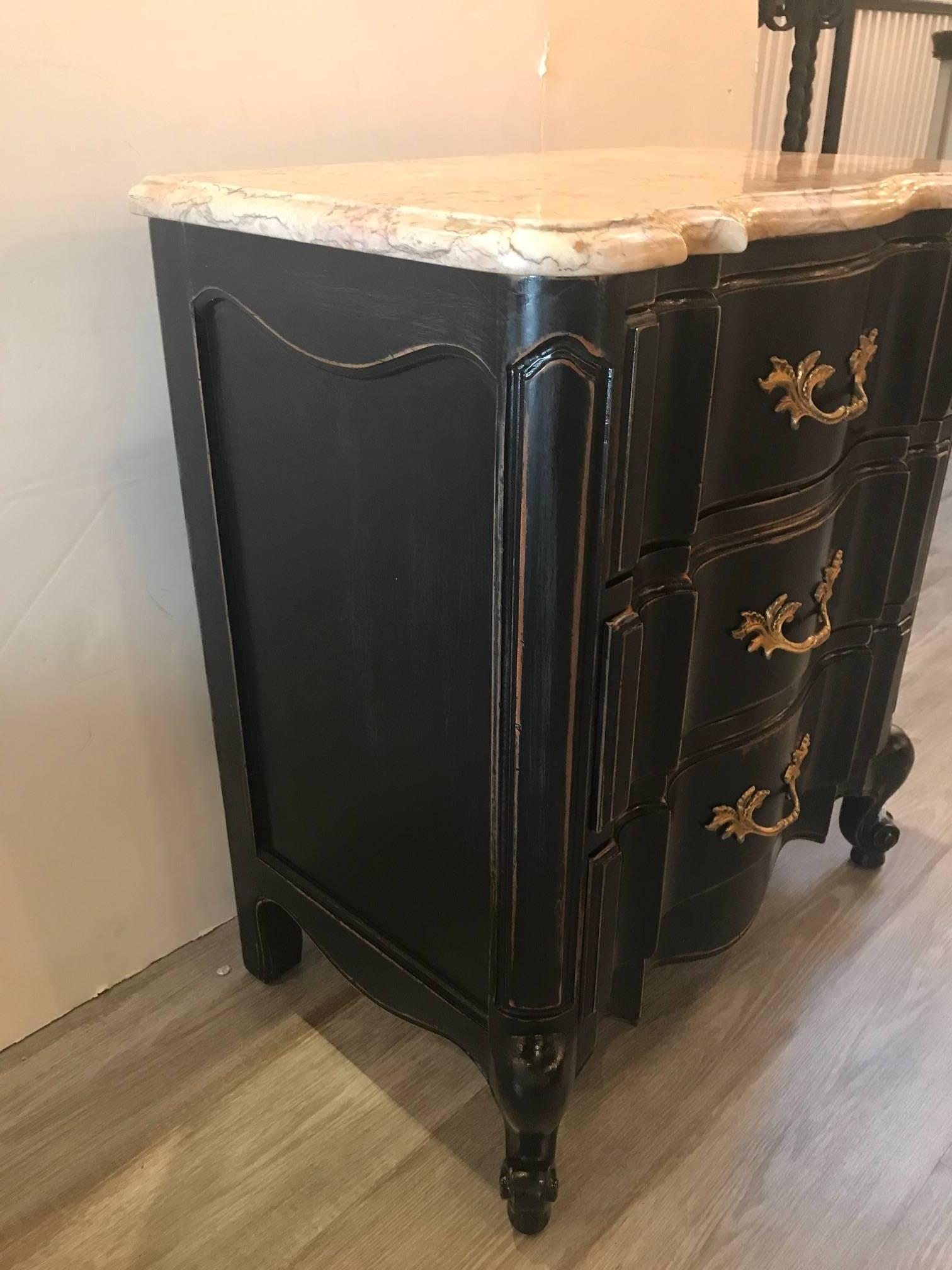 Shapely pair of French Provincial style drawer stands with original marble tops. The distressed black finish with cast brass handles featuring three drawers on each. One marble top has a professional repaired crack done well and blends beautifully.