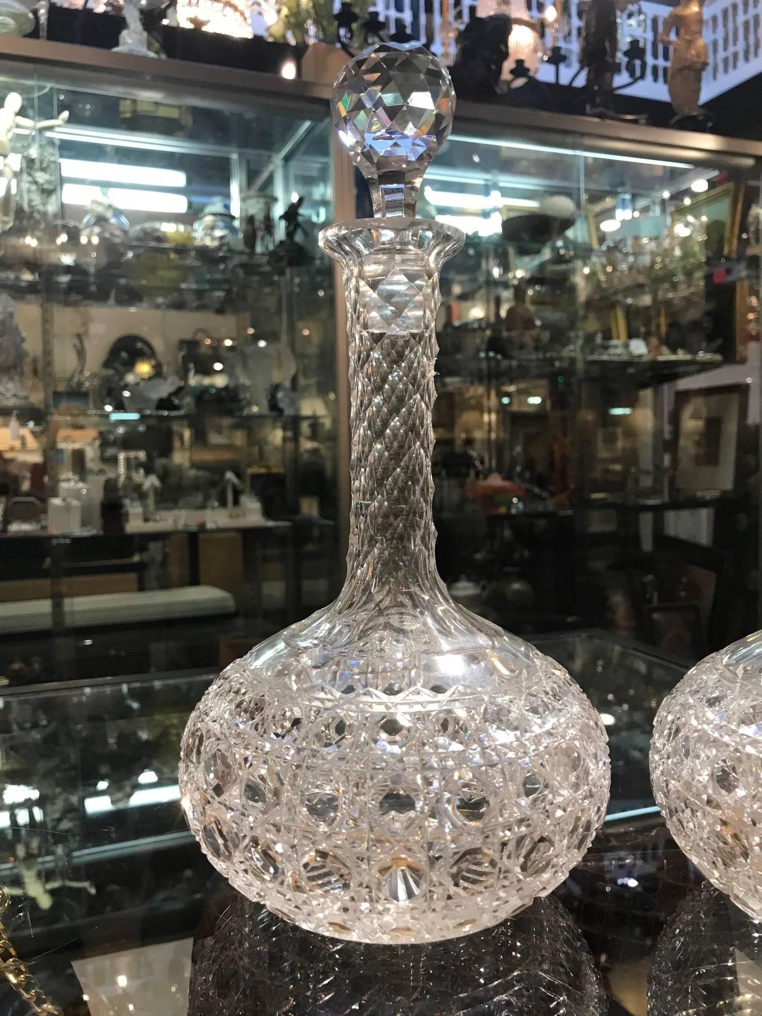 A shimmering pair of American hand-cut glass wine claret decanters with faceted stoppers. The bulbous bottoms with tall faceted necks and original ball facet stoppers. The body is in a Classic Russian cane pattern.