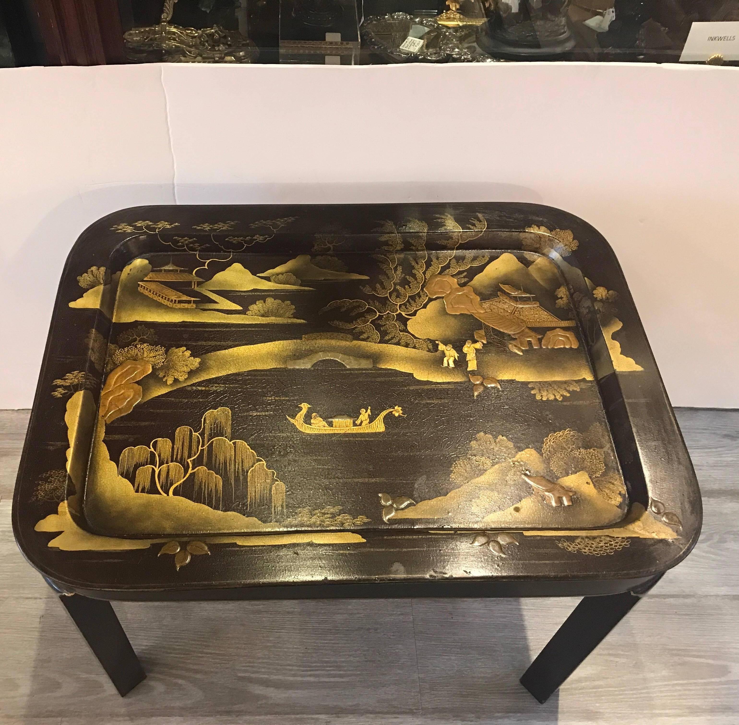 A diminutive tray top chinoiserie table. The lacquered removal tray with a rich brown background color with hand-painted gilt decoration. The Asian inspired base which is original to the tray.