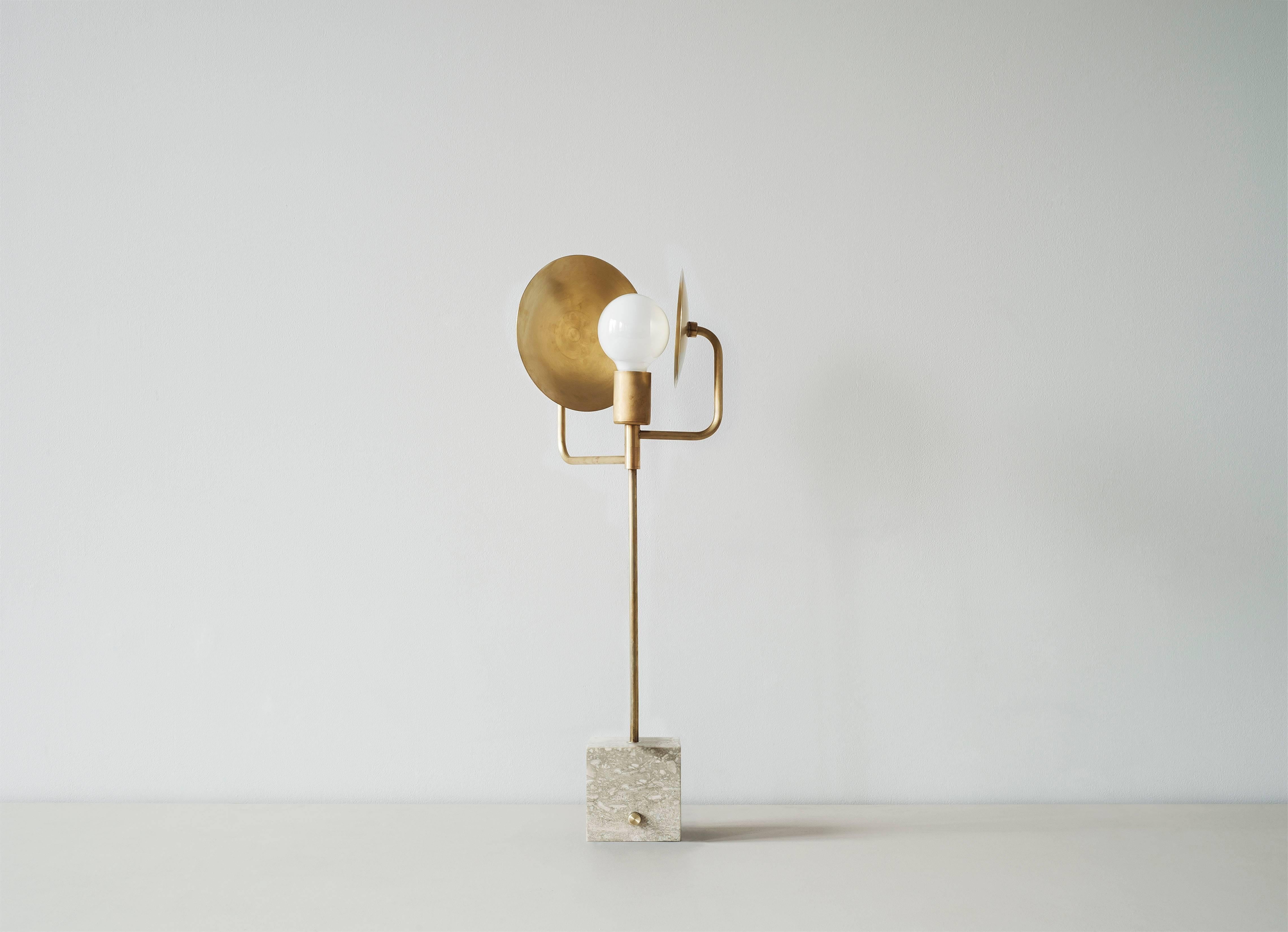 This table lamp features two spun brass discs which orbits like planets around a stationary bulb. With a base available in two varieties of stone, it is a grounded yet flexible piece for the tabletop. It can be arranged in a variety of