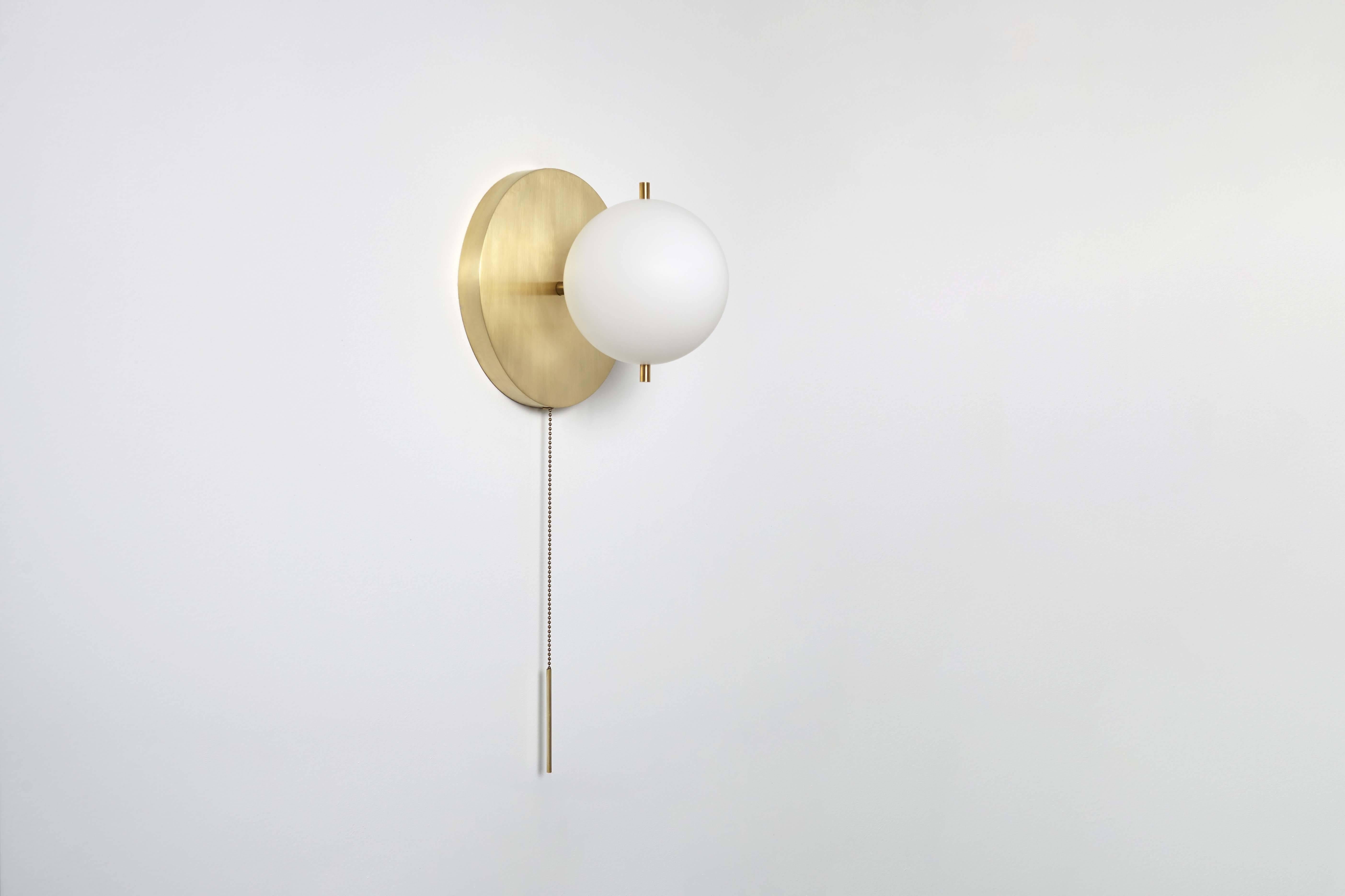 The signal sconce features a hand sanded globe. The fixture is delicately mounted between two metal pins above a luminous canopy, creating a hieroglyphic composition. A pull chain holds a slender rod, giving the piece a jewel-like presence. 