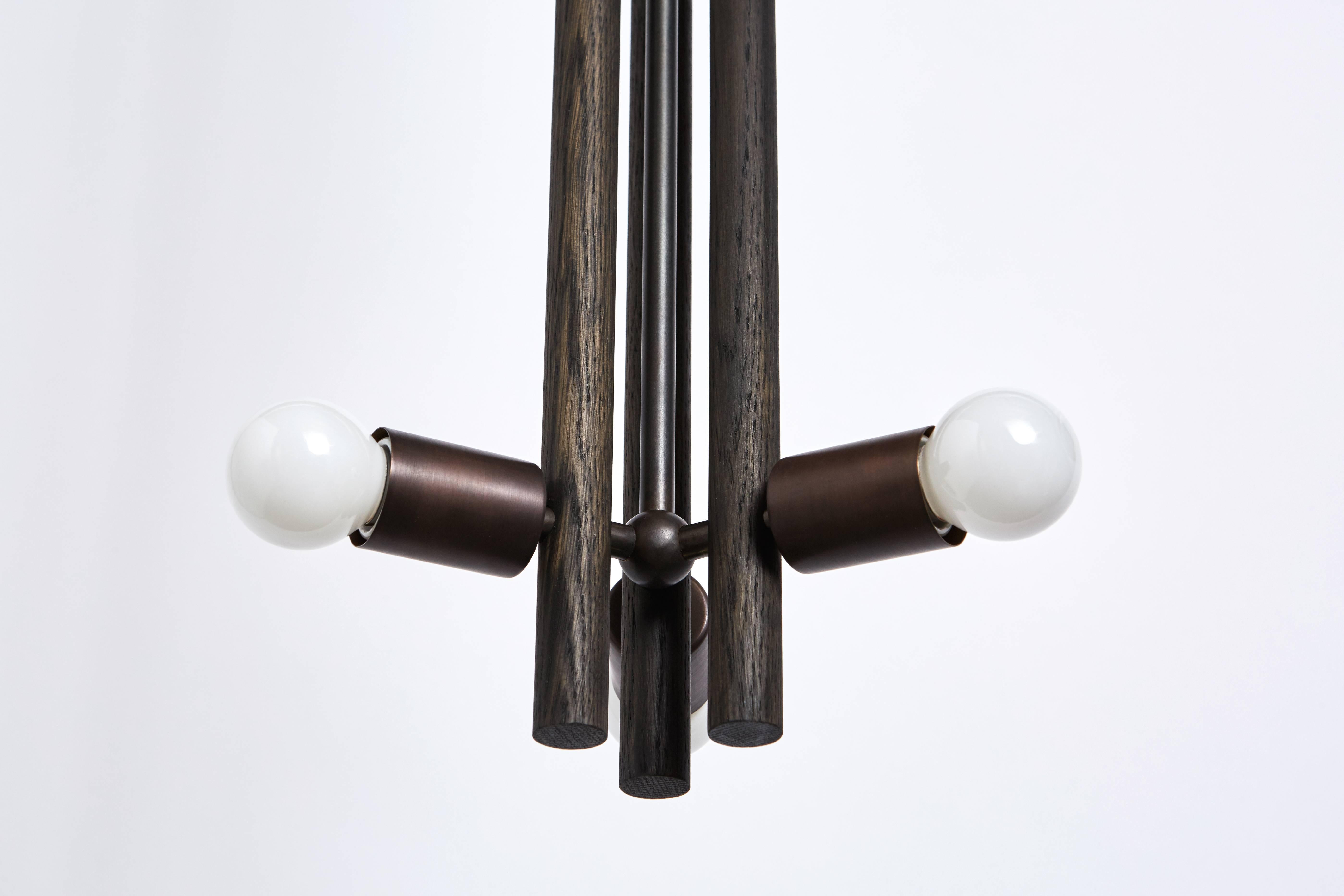 The lodge pendant is a singular wooden column, composed of three turned wooden forms. Held together by a network of metal tubing, with a milled metal ball connection, the bulbs radiate about the column.

Available in oxidized ash/blackened steel and