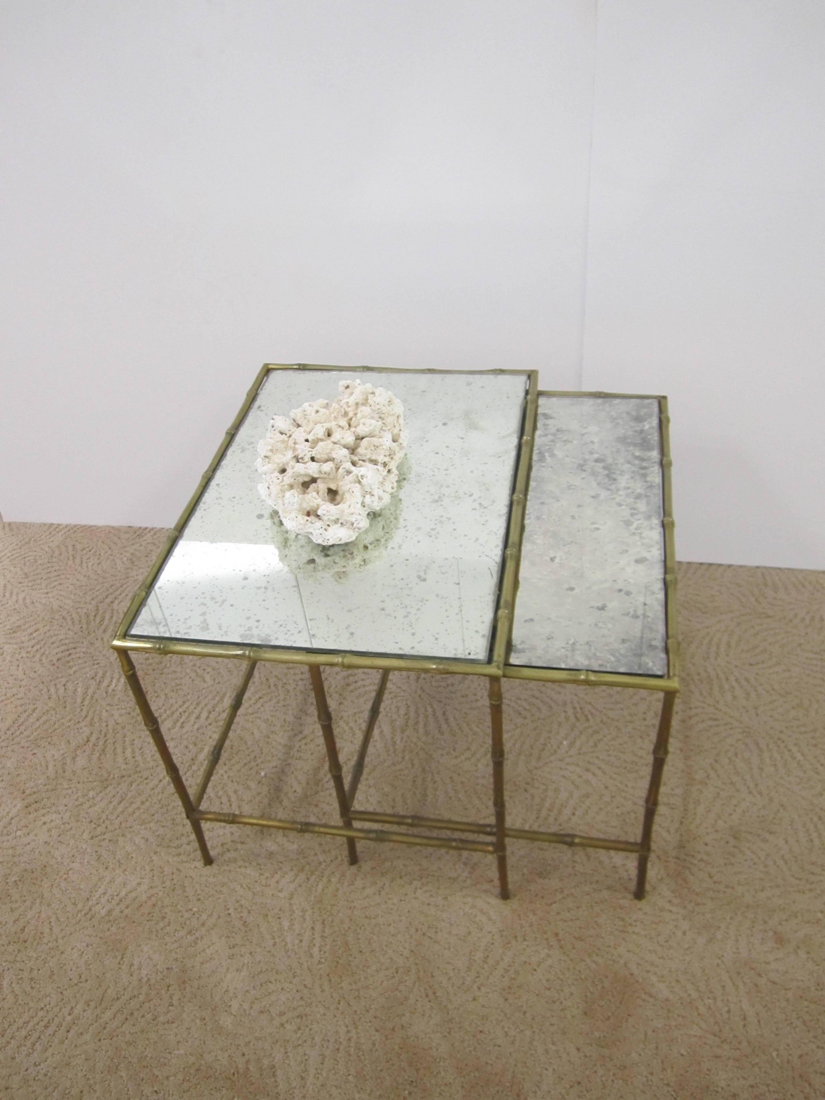 A beautiful and substantial pair/set of solid brass nesting, side, or end tables, circa mid-20th century, France. Brass frame has a 'bamboo' design and eglomise mirrored glass tops. Table style is attributed to French designer Maison Baguès.