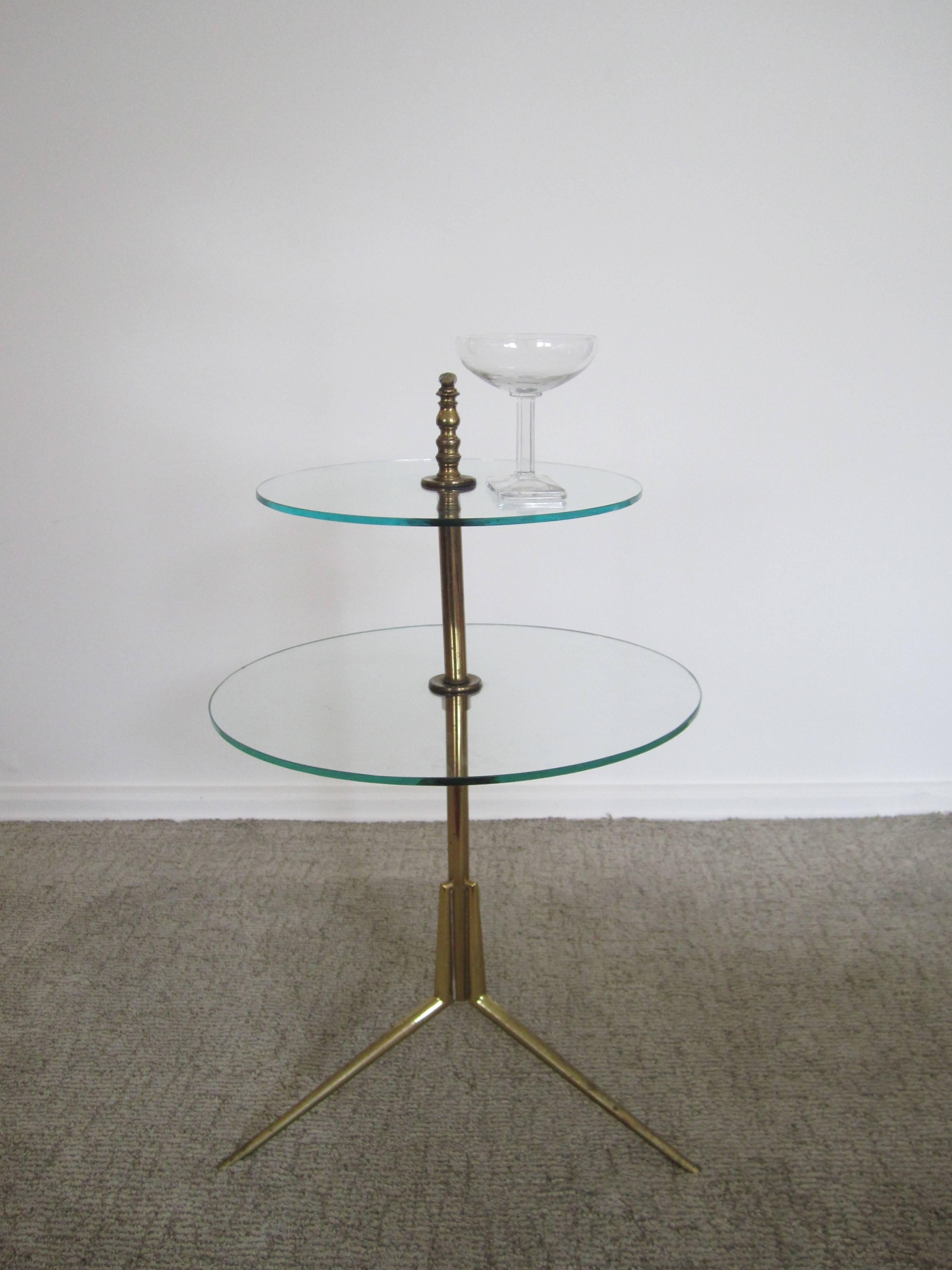 An Italian vintage Modern mid-century brass and glass two-tier side or drinks table with tripod base in the style of Italian designer Gio Ponti. Circa 1950s-1960s. Item available here online. By request, item can be made available by appointment to