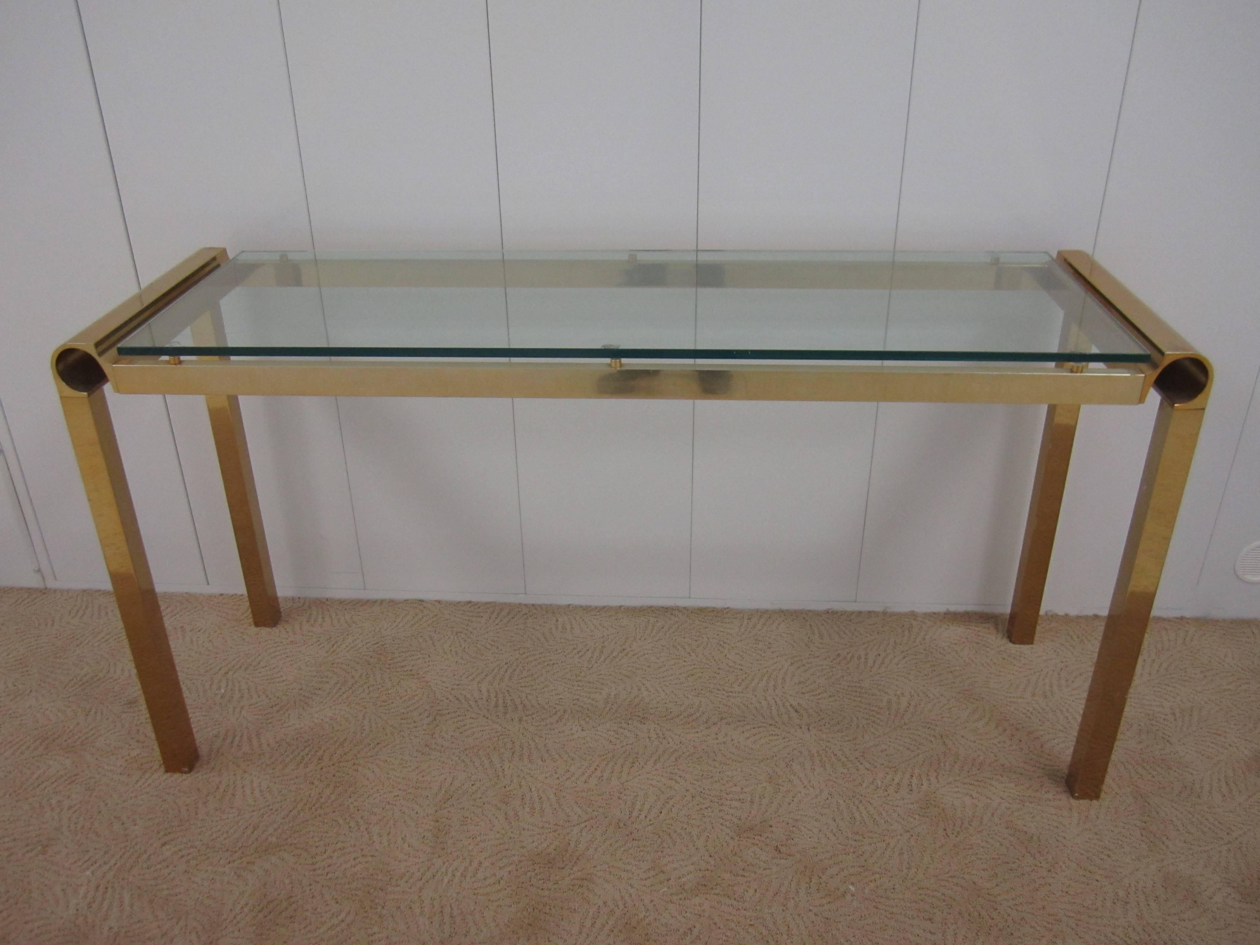 1970s Modern brass and glass console table in the style of Pierre Cardin. Half inch thick floating glass top. Brass top with 'C' curve detail and square brass-plated legs. 