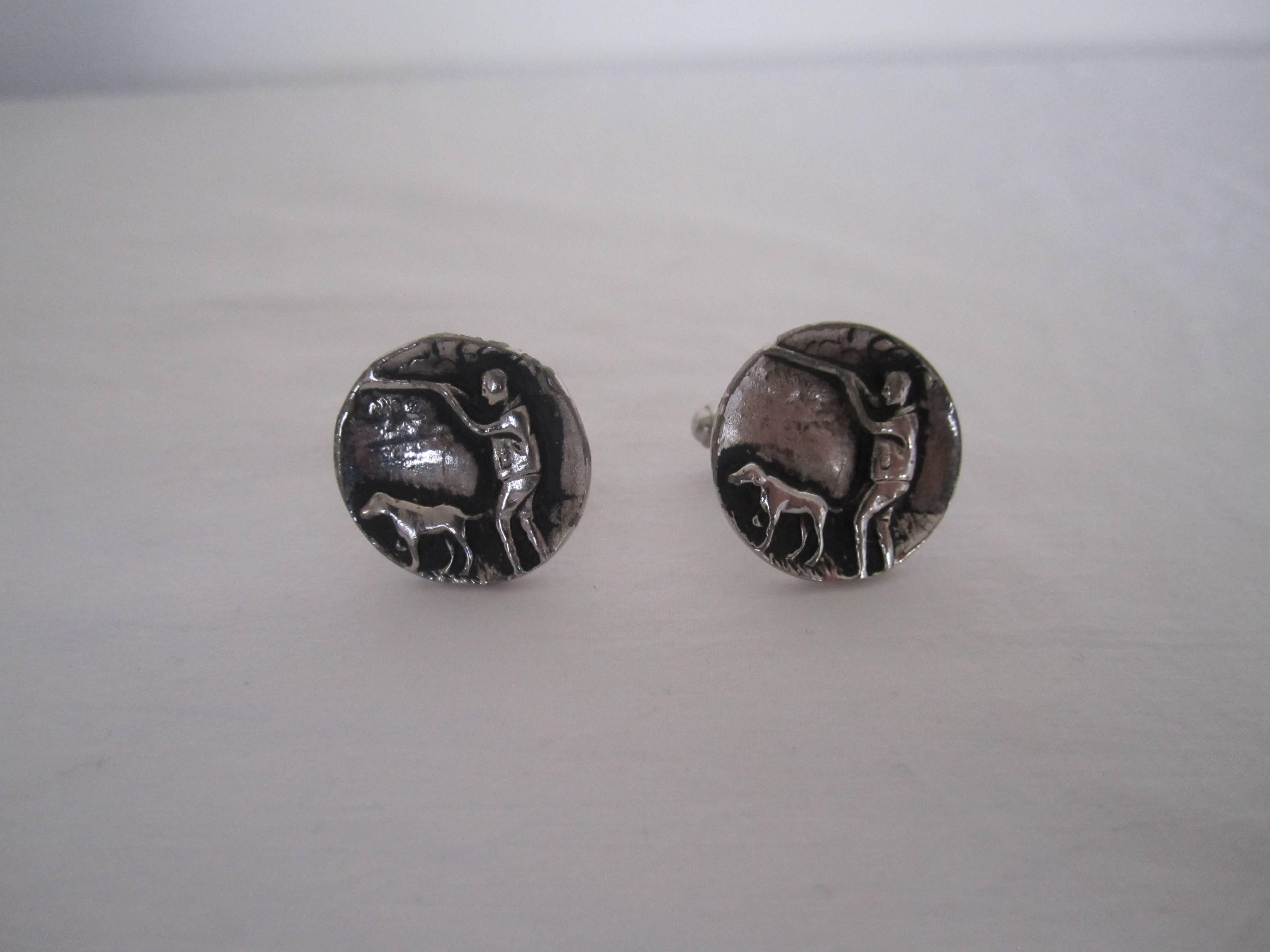A unique pair of 'Hunter and Bloodhound Dog' cufflinks in a silver tone metal. 
Each measure .75 inch in diameter.
