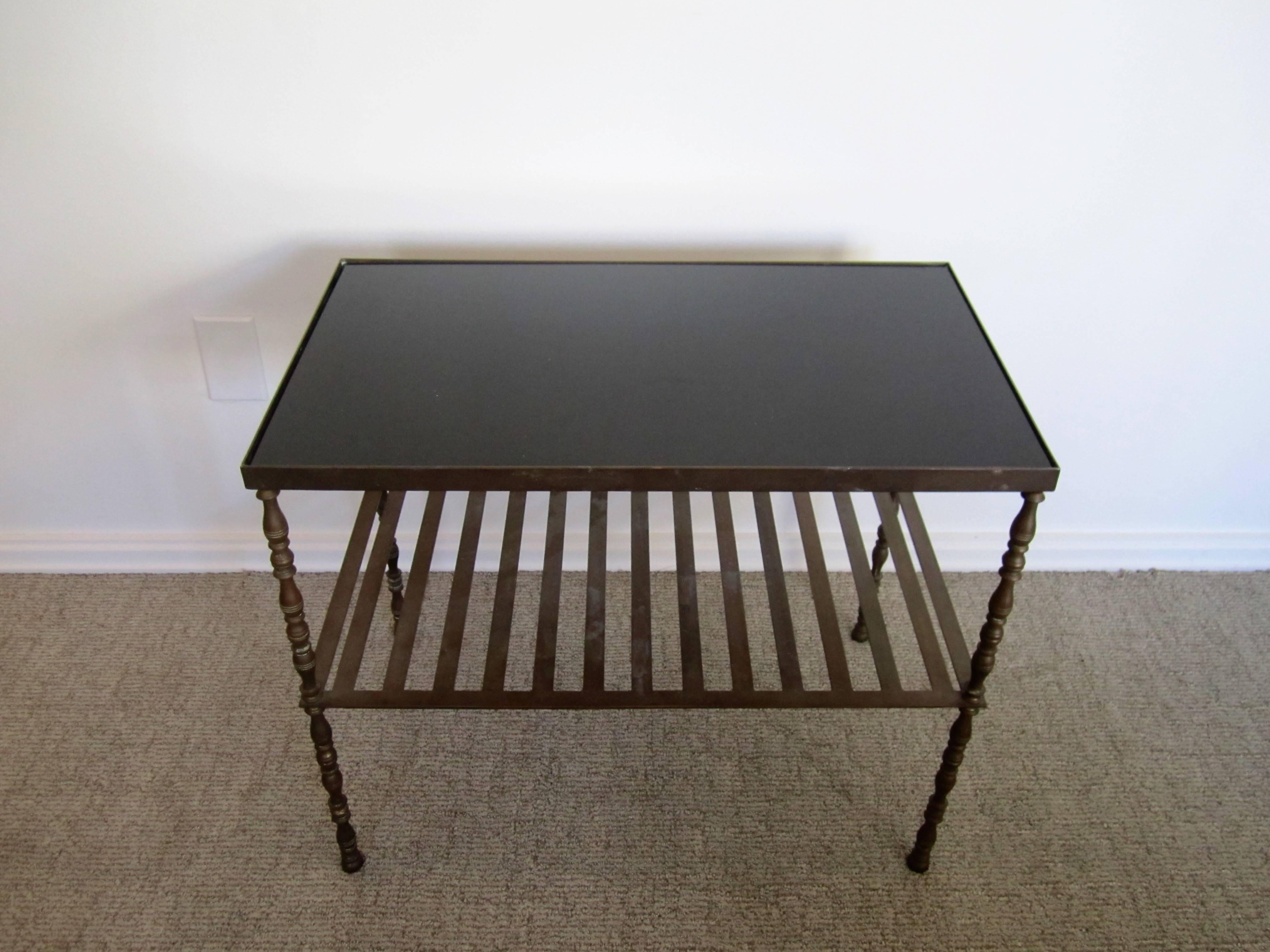 A Mid-Century French vintage bronze table that can double as an end or cocktail table, bookcase, or bar. This rectangular bronze table has a black glass top, spindle legs, and lower slatted shelf. Glass top is inset. Measurements include: 20' h x