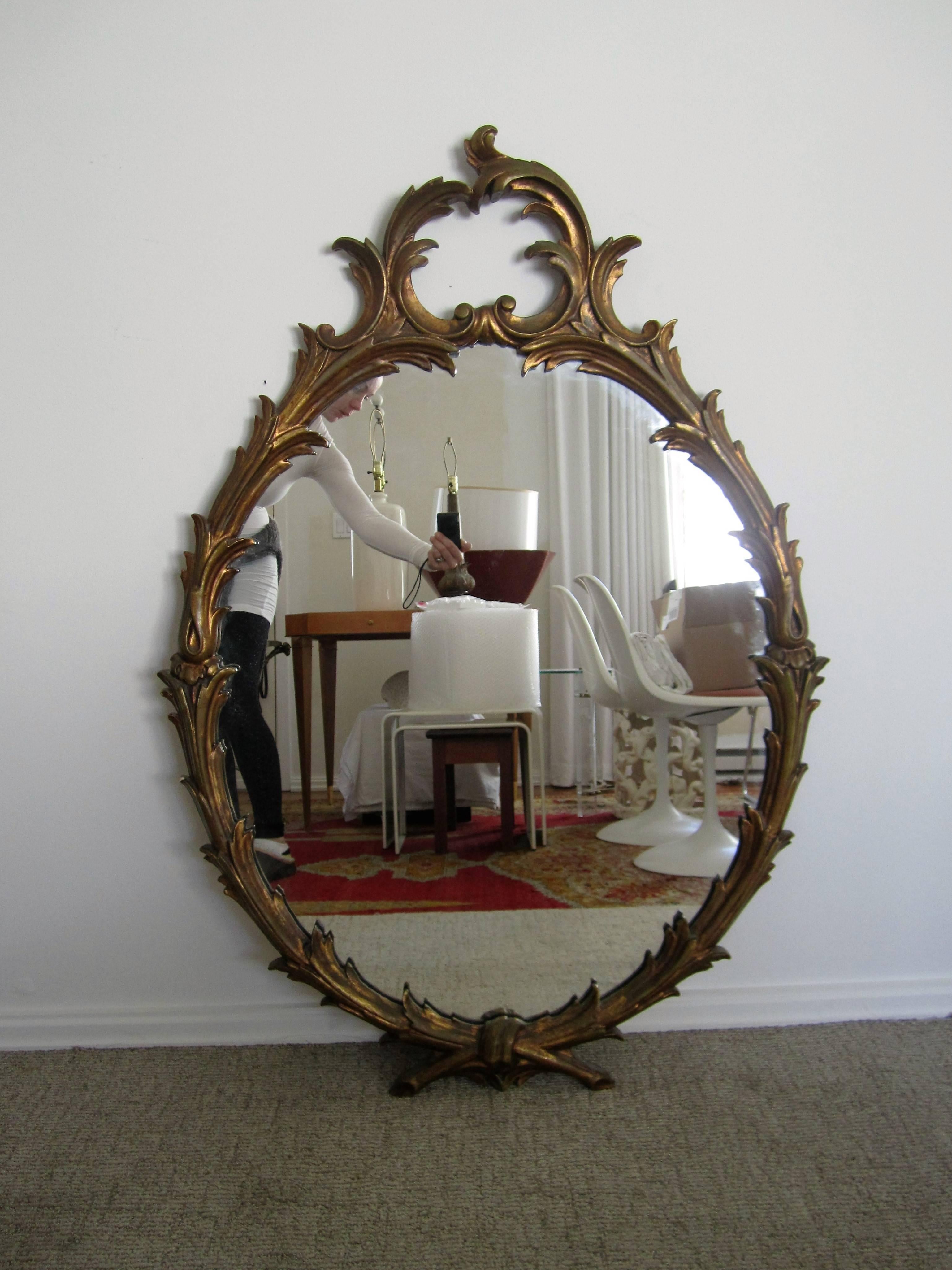 A substantial vintage oval Italian gold giltwood carved wall mirror with a vine design, circa mid-20th century, Italy. Marked 