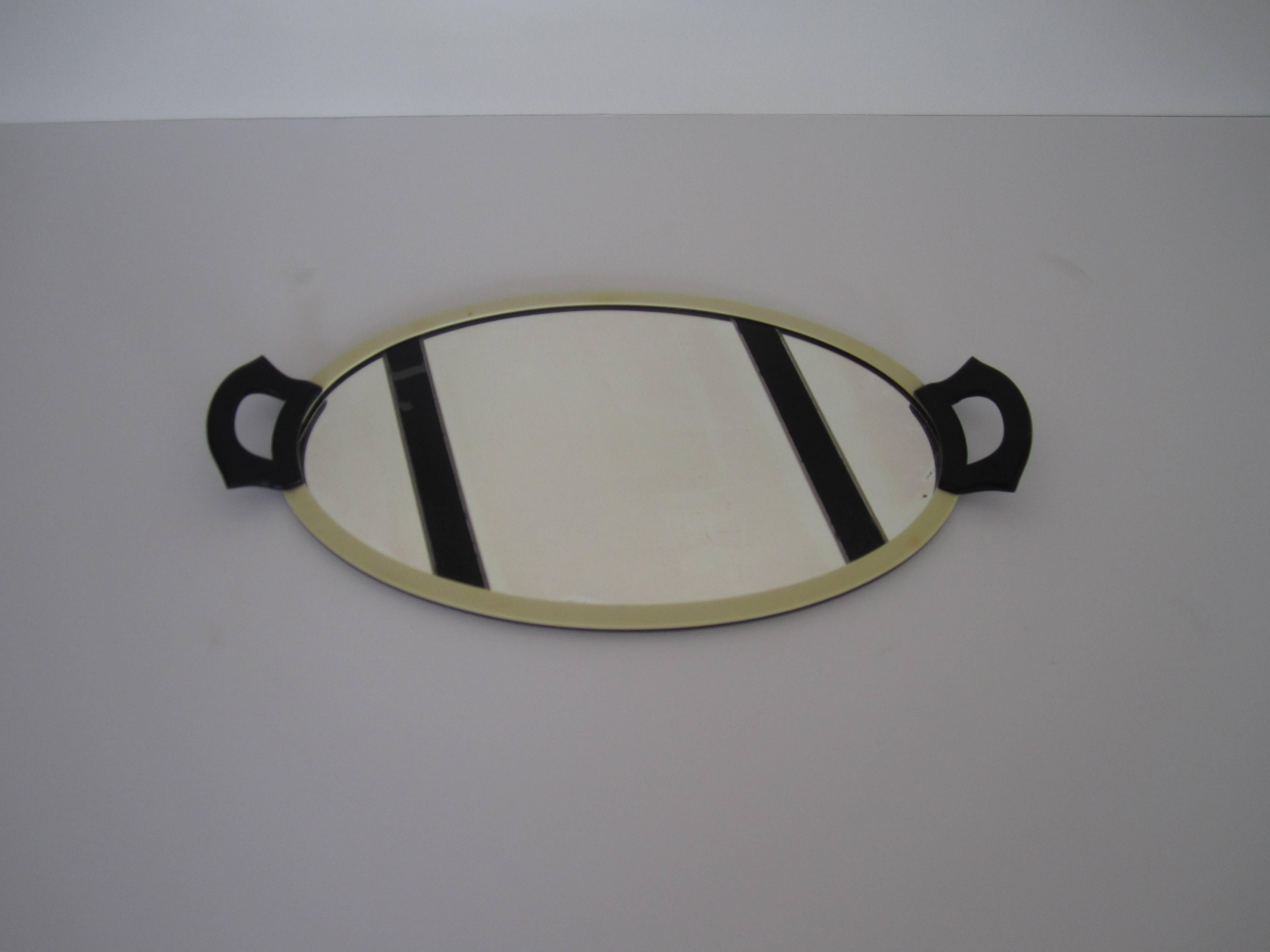 An oval French Art Deco period mirrored vanity tray with black decorative stripes, black Bakelite handles, and an ivory colored celluloid frame, circa 1930s. 

Item available here online and by request, can be made available by appointment to the