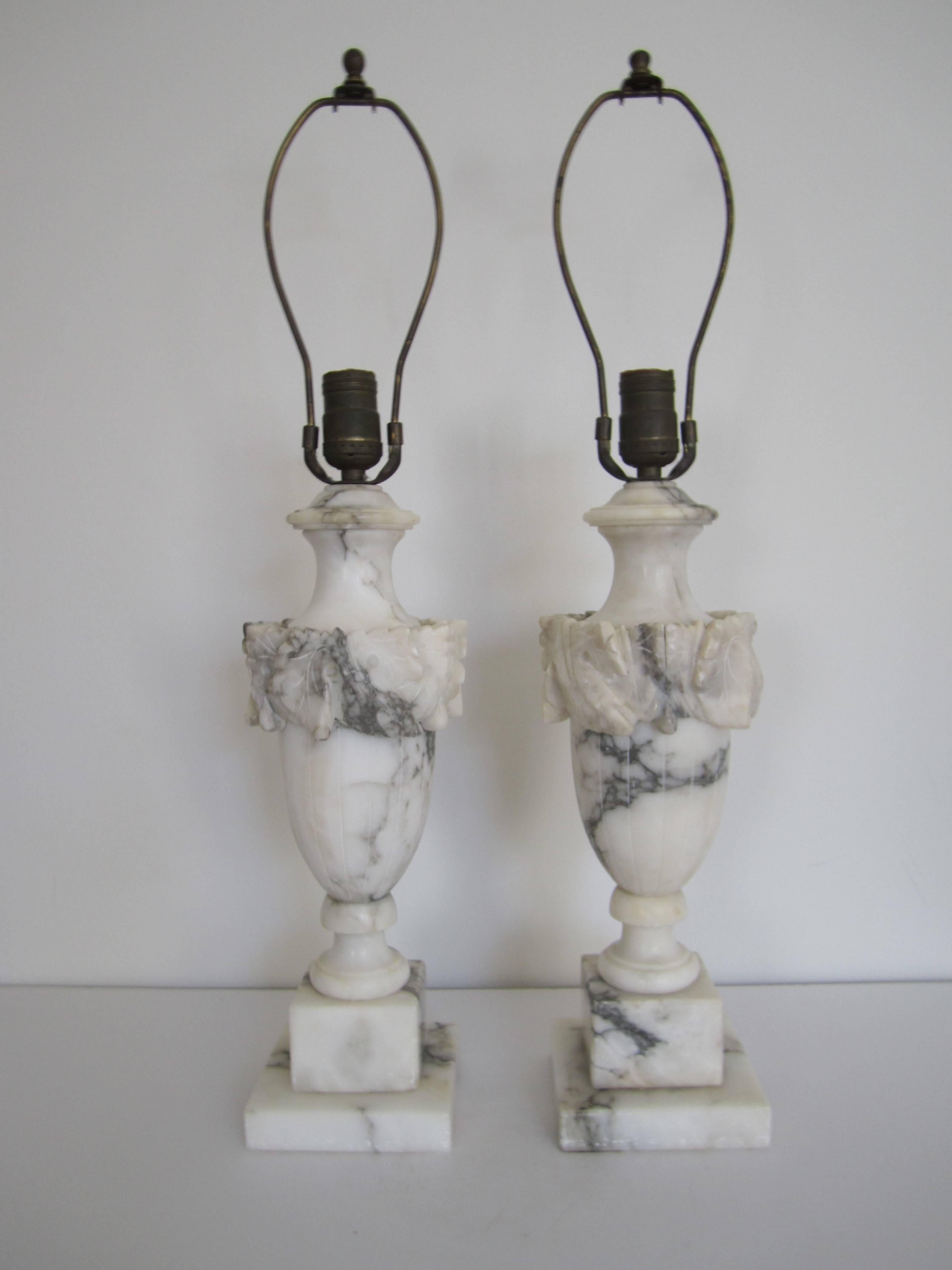 A beautiful pair of Italian Neoclassical style urn form carved solid Carrara marble table lamps, circa early 20th Century, Italy. Marble (Carrara marble) is predominantly white with black and gray veining throughout. Shown with black shade and white