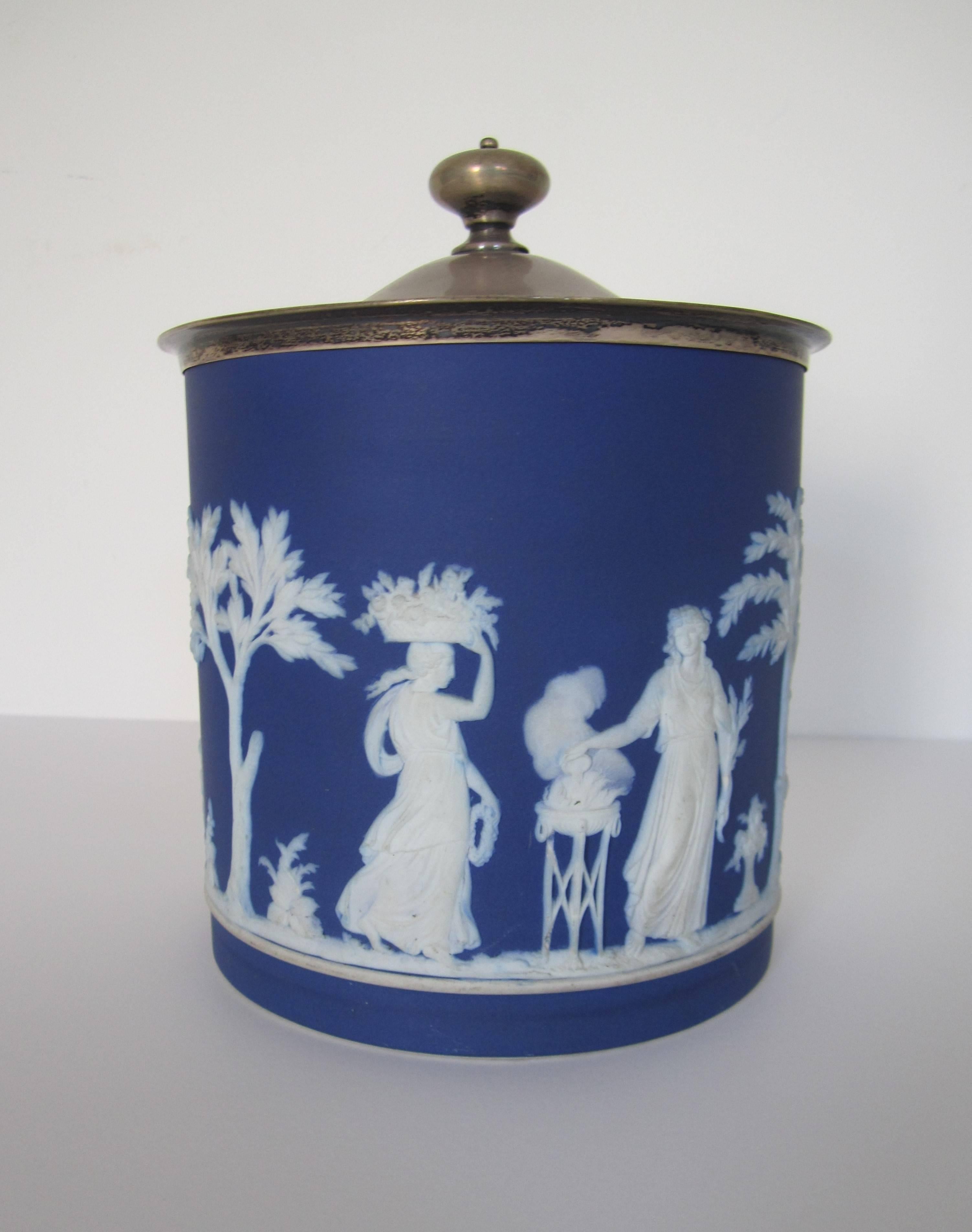 A beautiful antique Wedgwood Jasperware cobalt blue and white vessel with sterling silver plated lid. Made in England. A stunning detailed raised relief around a matte unglazed stoneware vessel with sterling silver plated cover or lid. With maker's