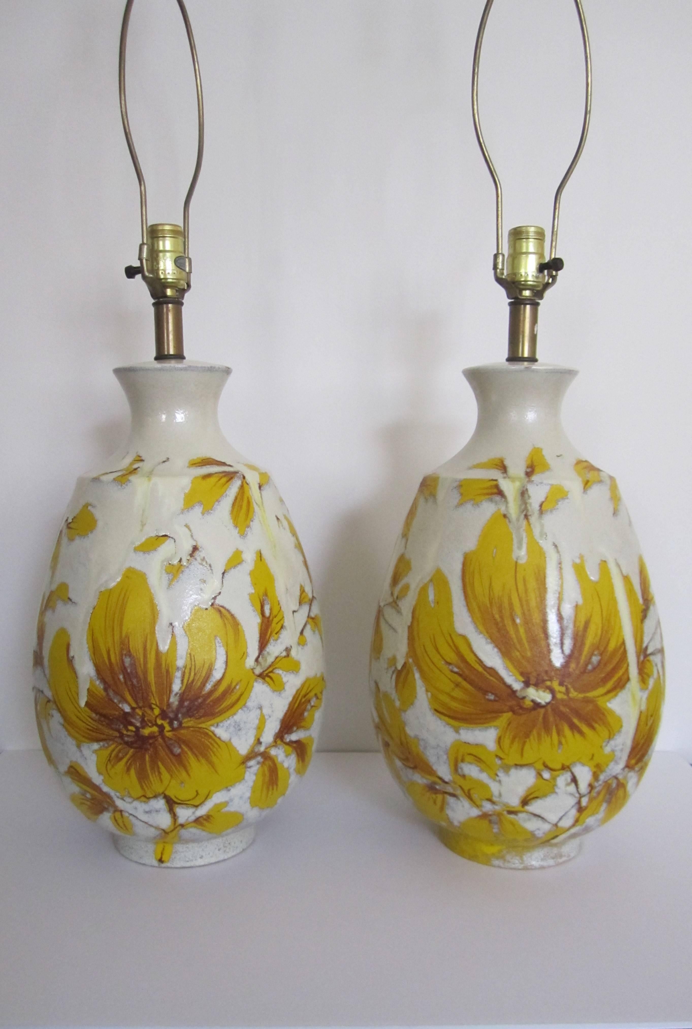 A stunning pair of relatively large yellow and white terracotta pottery table lamps, circa mid-20th century, 1960s. Lamps have large floral motif on front and smaller flowerets on side and back, finished with a textured surface. Colors include