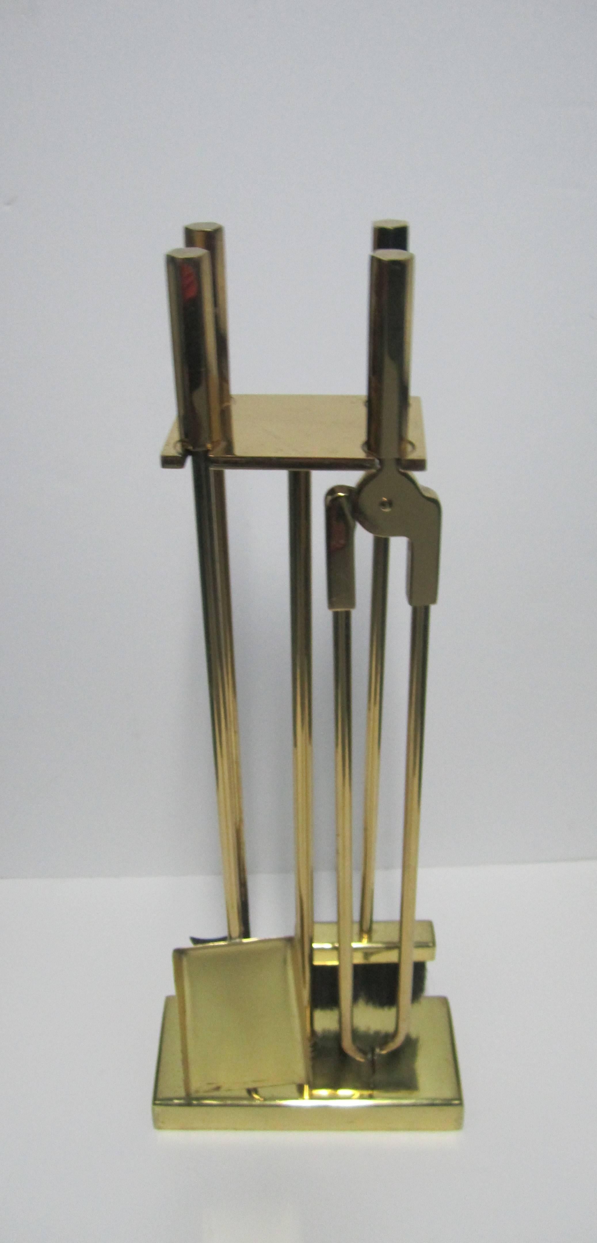 A substantial Modern style brass fireplace tool set. Set includes four tools with 'hexagon' shape handles held floating by rectangular base frame. Tools sit square with two in front and two in back. 

