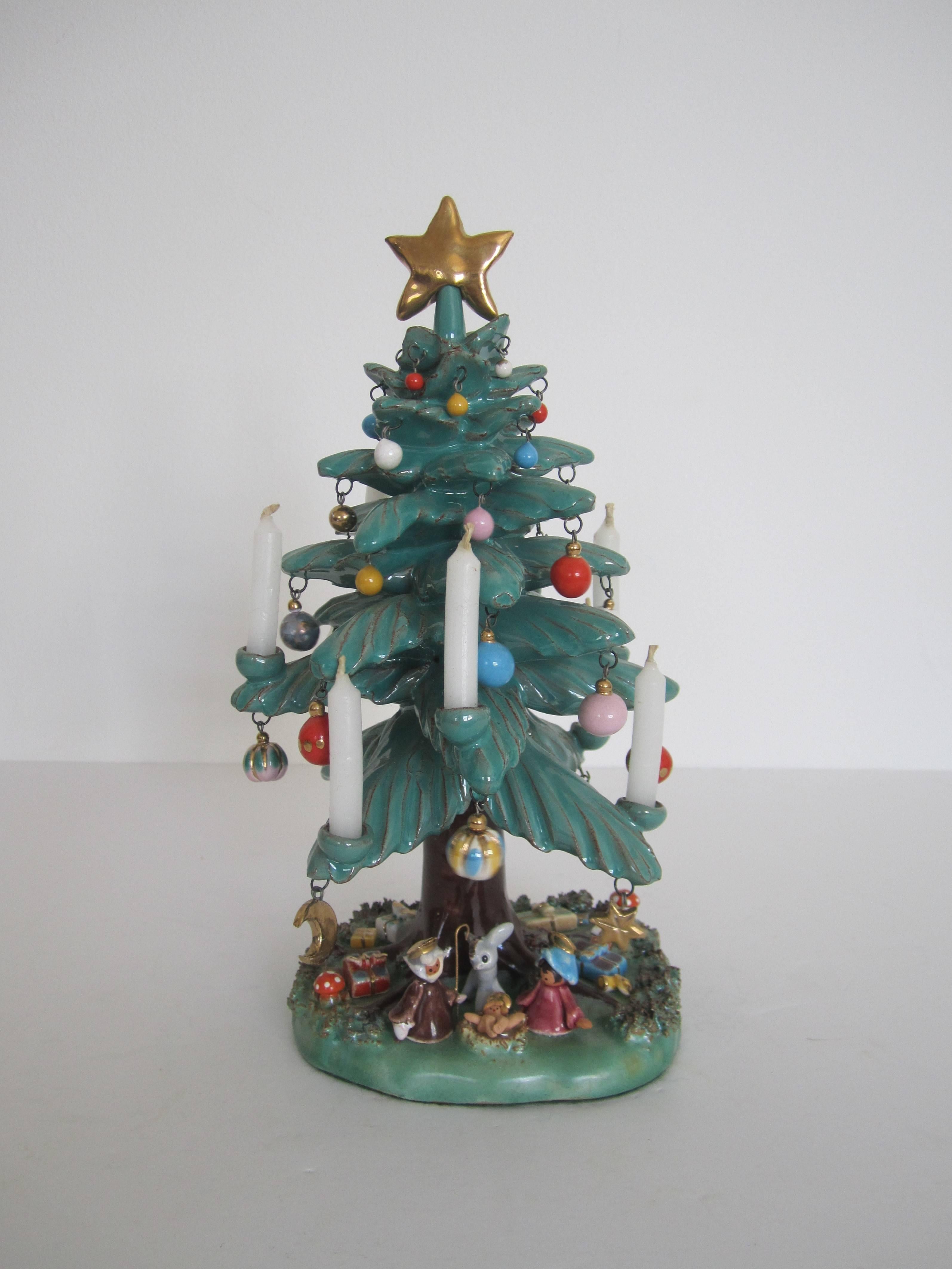 A stunning vintage Mexican pottery Christmas tree sculpture with nativity scene. Christmas tree has eight candleholders around tree that hold small birthday size candles, many gold and colorful detailed dangling Christmas ornaments, large gold star