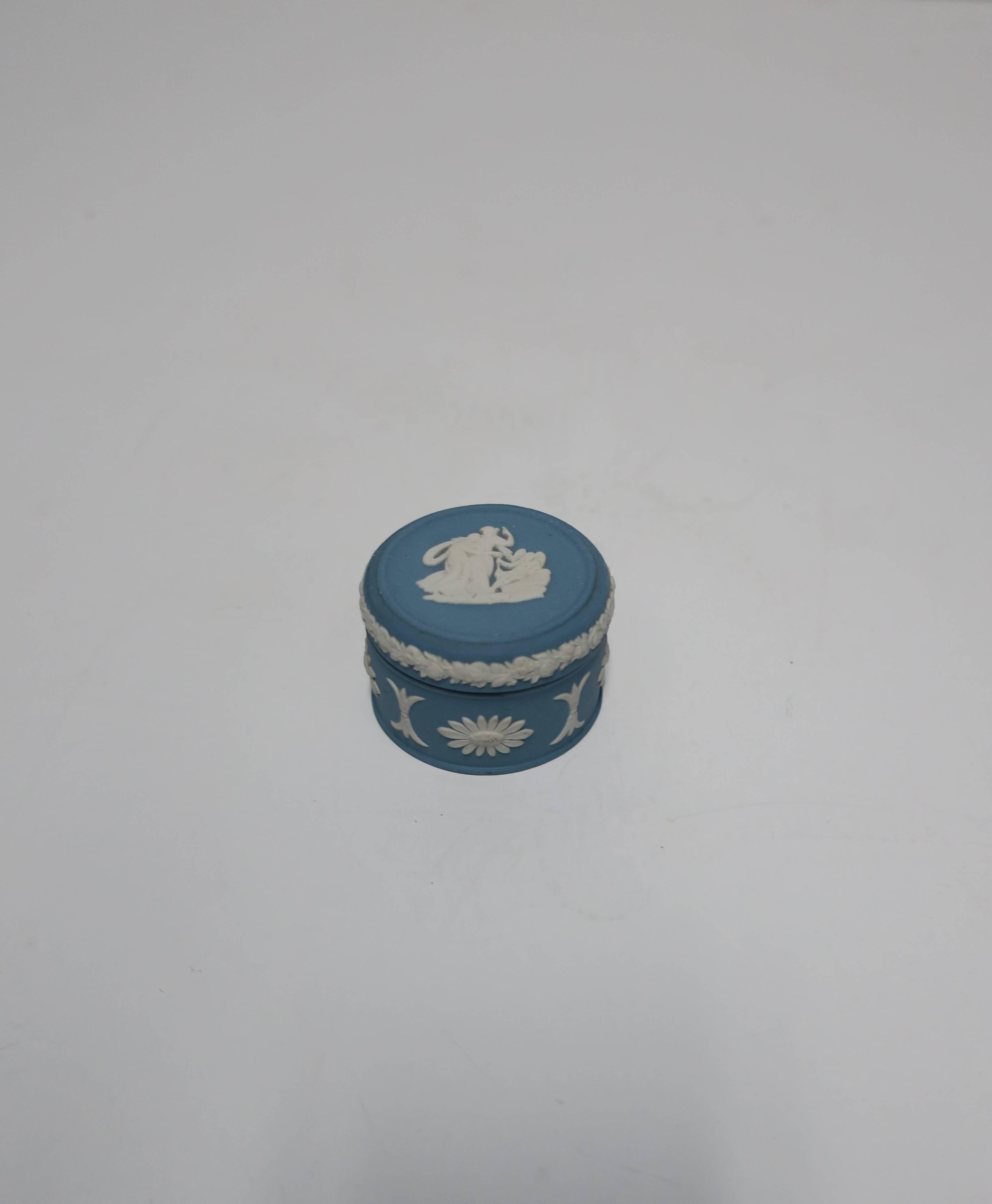 A beautiful petite Wedgwood Jasperware small round trinket or jewelry box. Box is a blue and white matte unglazed stoneware with raised relief around outside and on top. With maker's marks on bottom as show in image. Made in England.