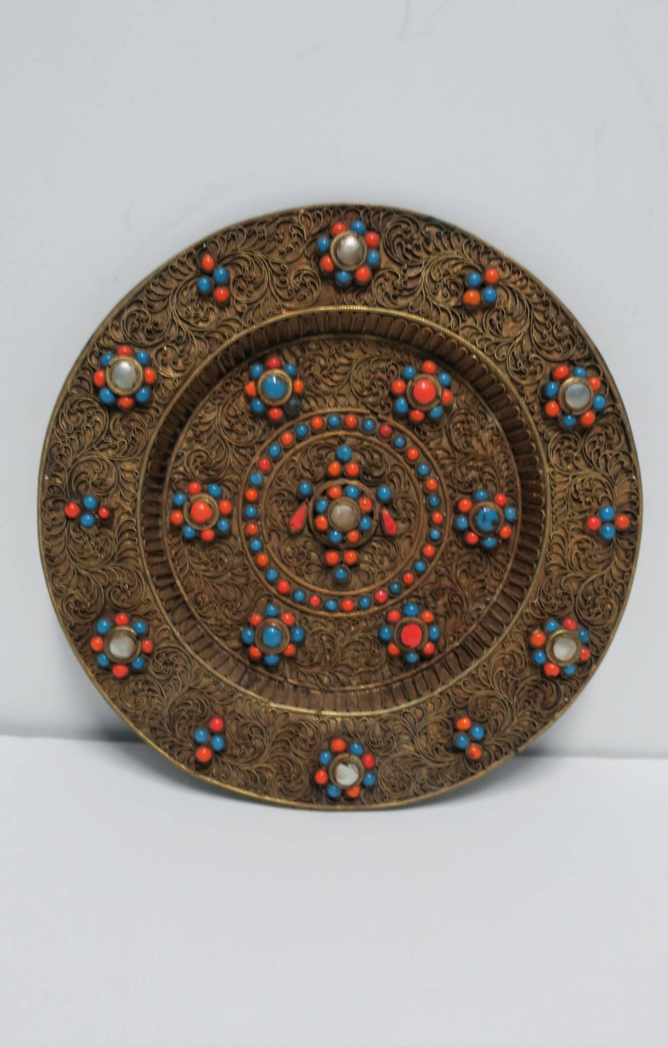 A beautiful decorative brass wall plate of mother-of-pearl, orange coral, and blue turquoise cabochon elements, circa 20th Century, Nepal. Plate has round hook on back for hanging. Inscribed on back, 