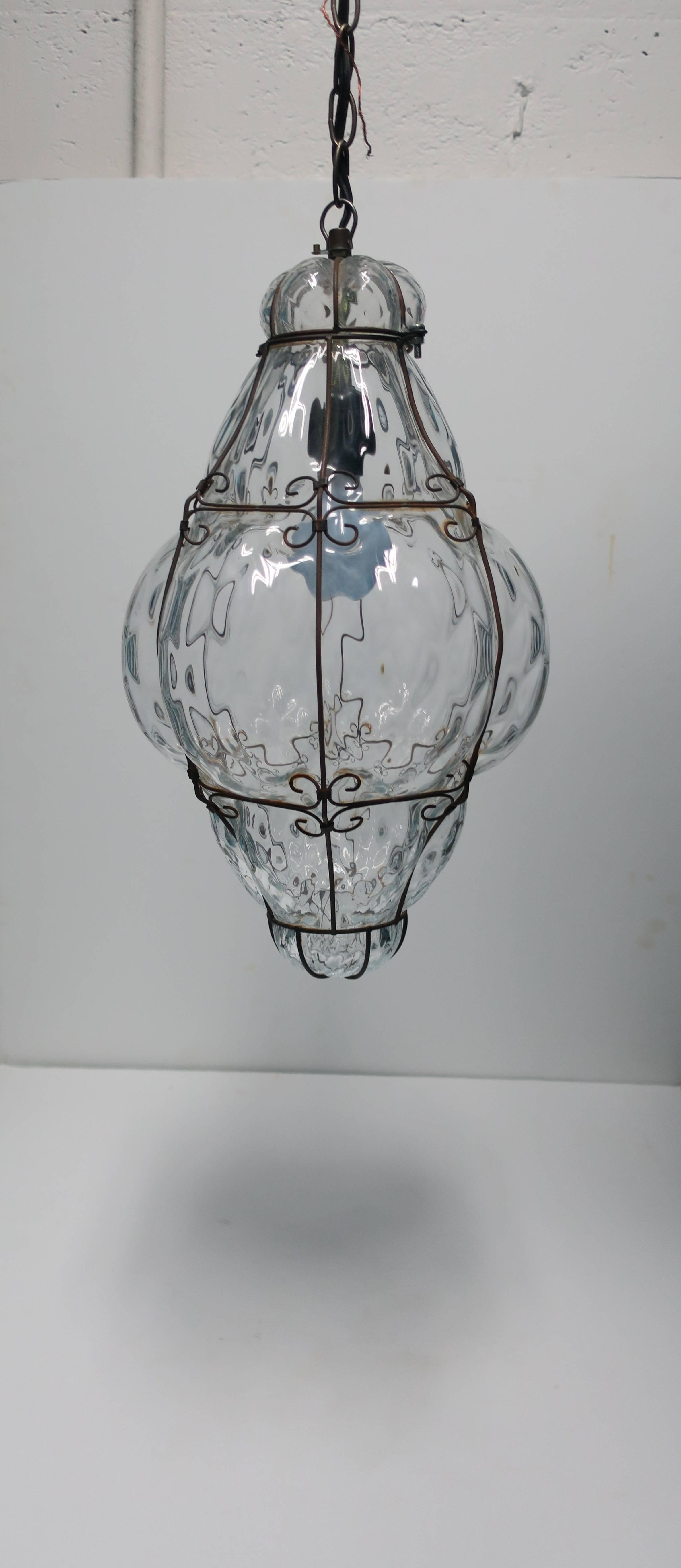 A relatively large, clear, Italian one lamp/bulb lantern pendant hand-blown glass light embraced by decorative metal, Italy, circa 1950s, Italy. In working order. 

Measurements include: 19.5