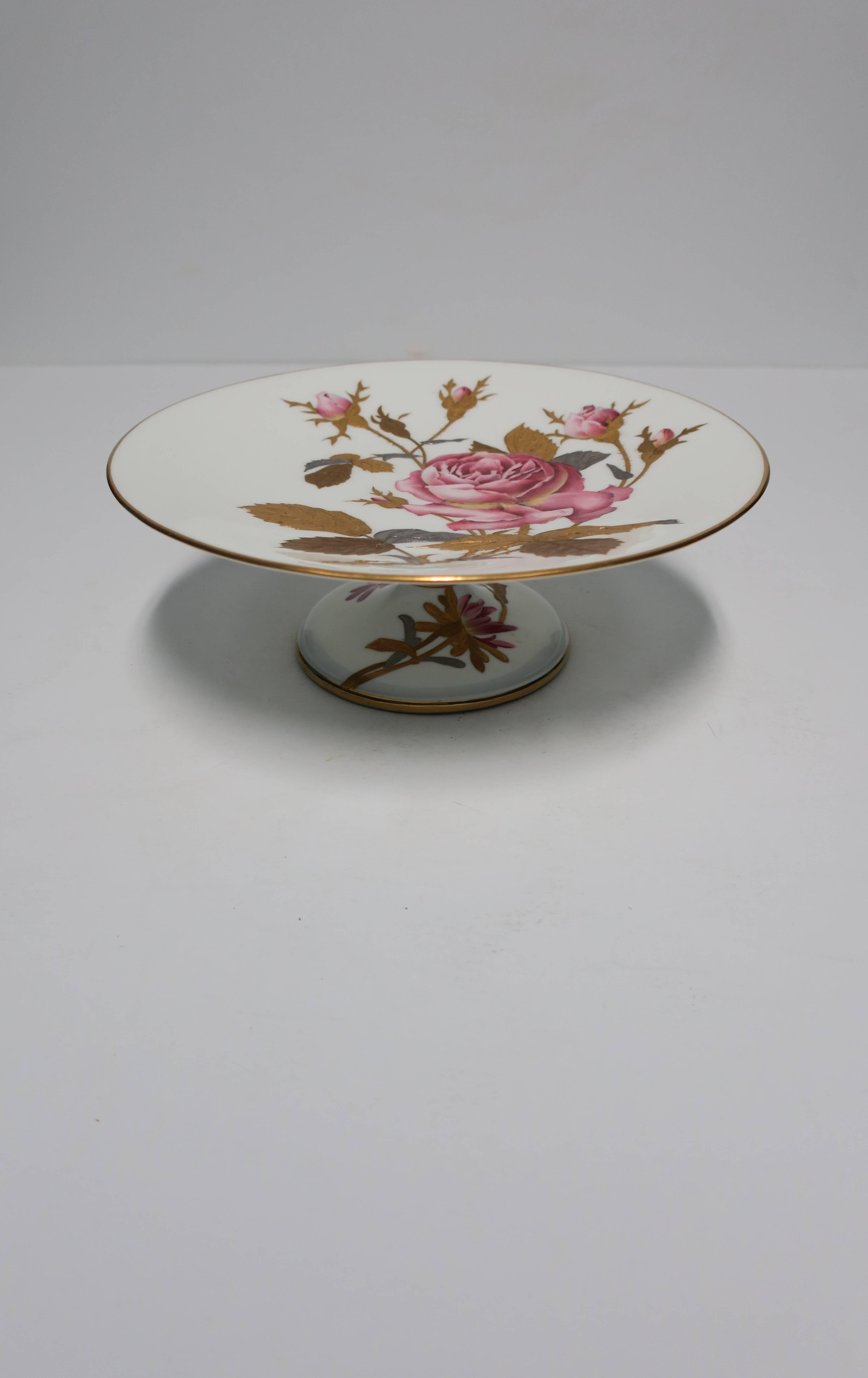 A beautiful European porcelain pedestal compote or dessert / cake plate stand, circa mid-20th century, Europe. Piece is hand painted with pink roses, generously raised gilt in gold, silver, and copper leaves, finished with a gold trim around edge