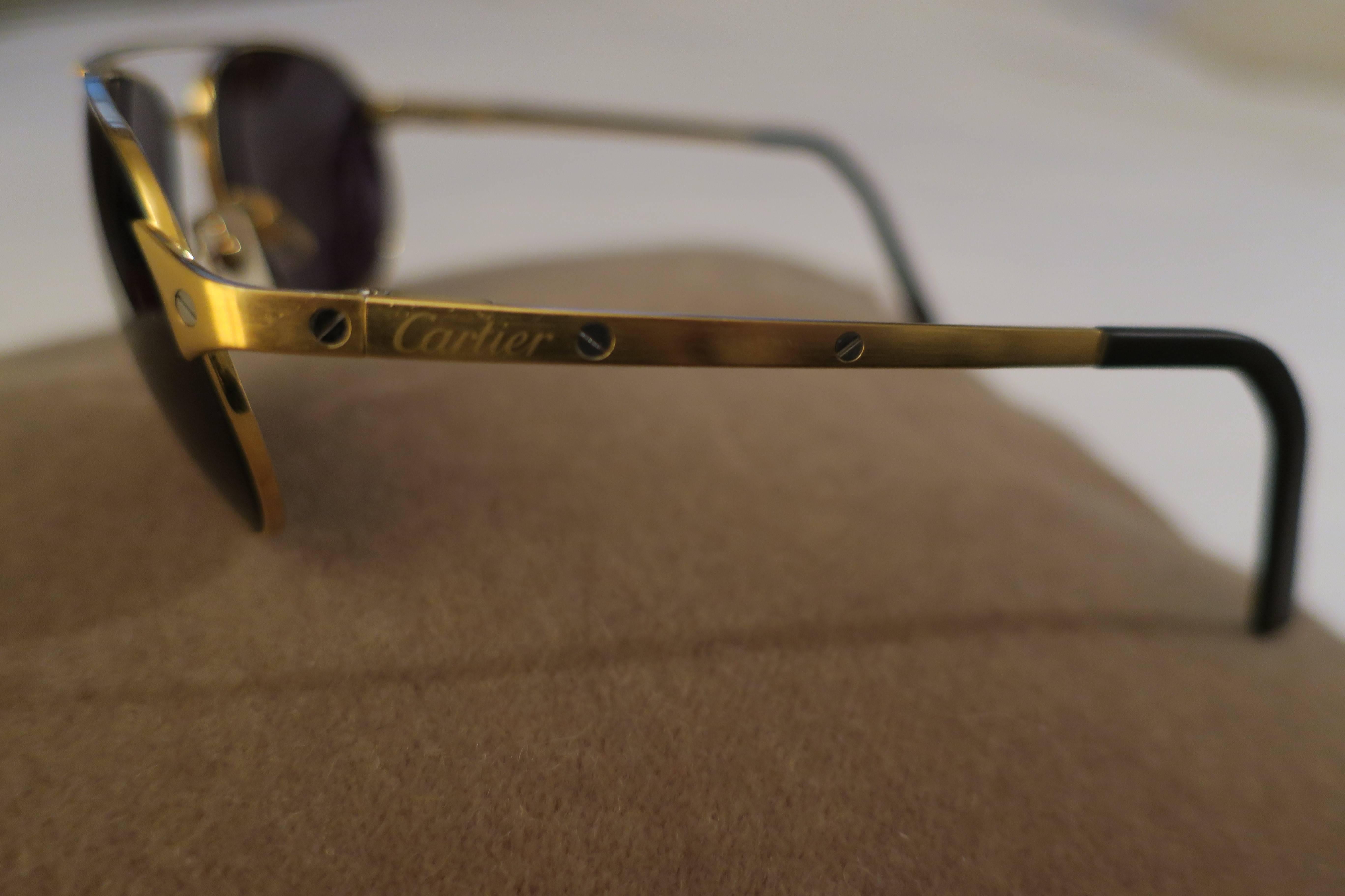 A beautiful and classic pair of authentic Cartier Santos aviator sunglasses with gold metal frame designed with the iconic 'Santo' screw detail. Sunglasses have polarized and custom dark lens for protection and privacy. Marker's mark: 