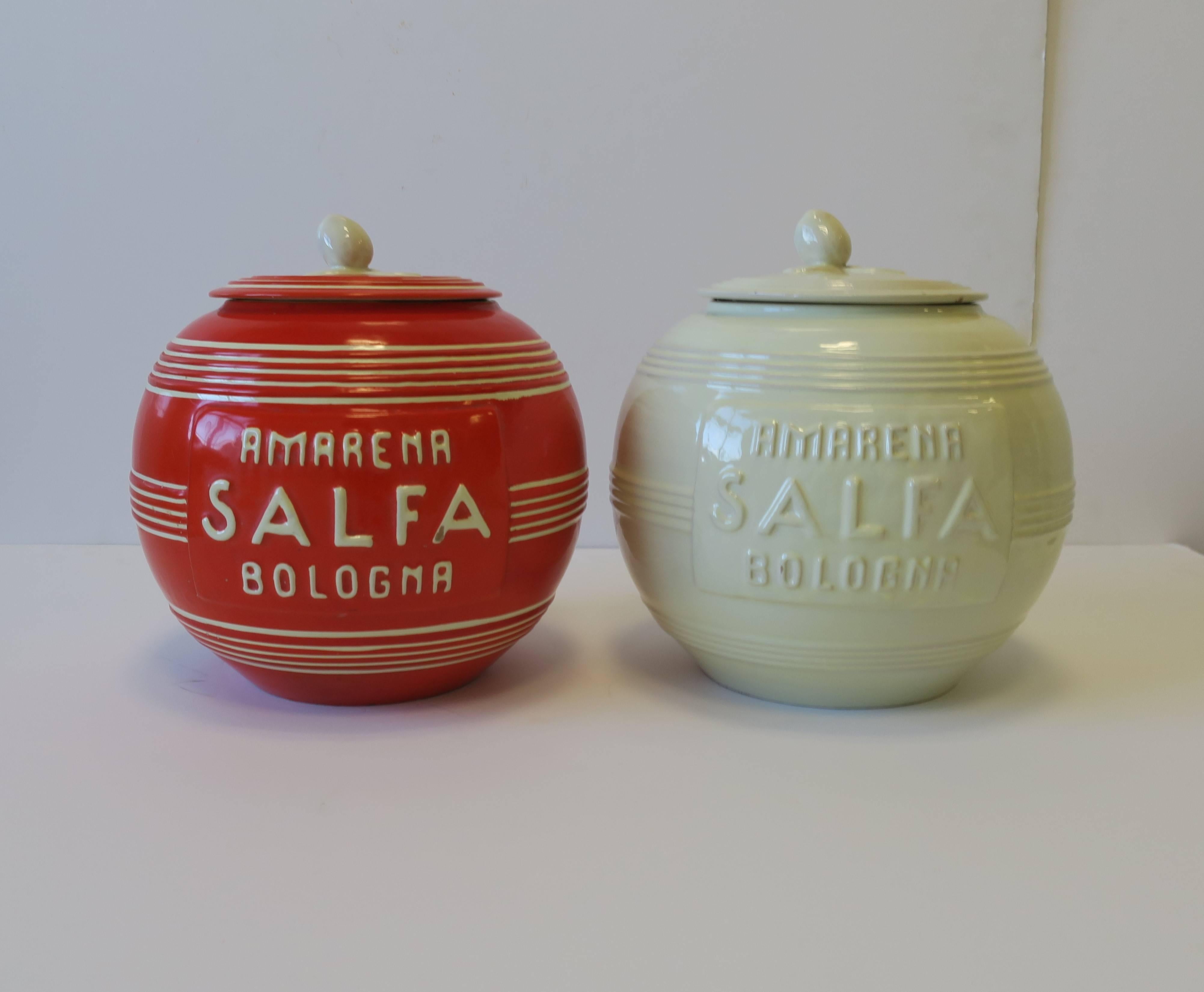 A beautiful set of two (2) Italian Modern Art Deco period pottery jars/vessels, circa 1930s, Italy. Copy/text reads: AMARENA SALFA BOLOGNA. One is designed in a beautiful orange hue with cream or off-white accent color, and the other a solid cream