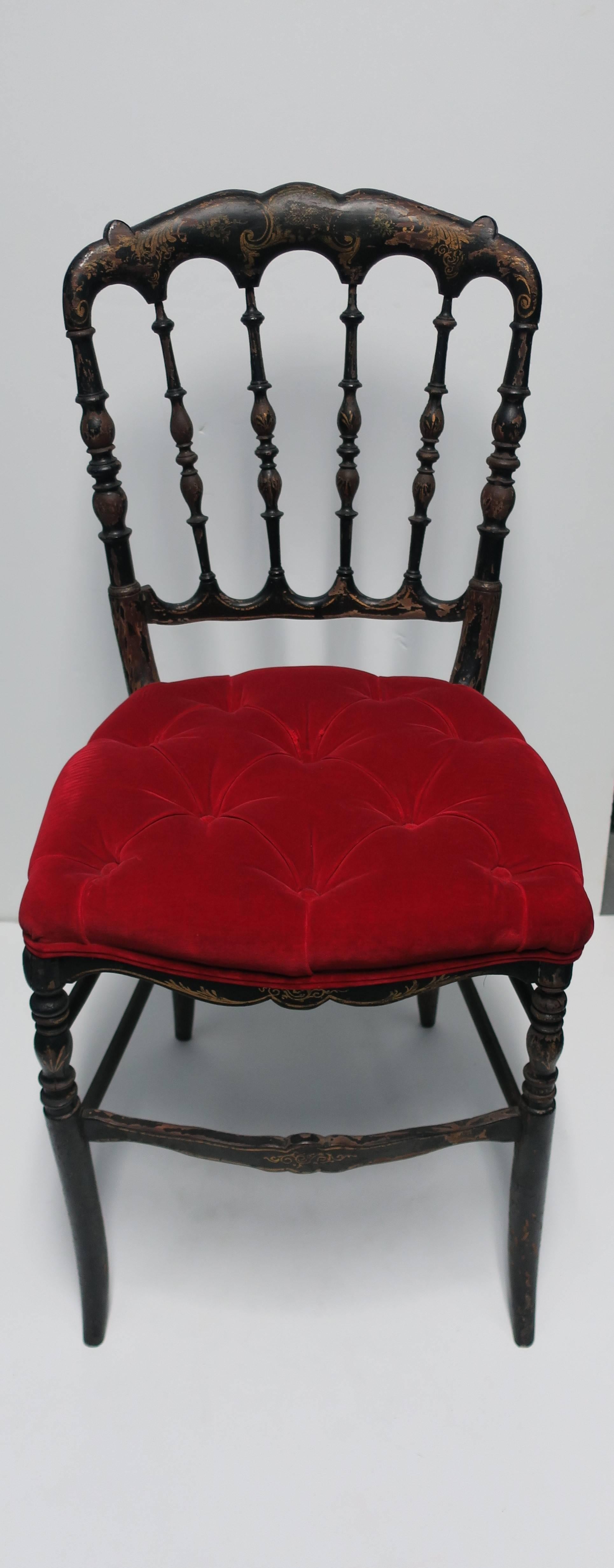 An antique English Chiavari black wood painted side chair with striking red velvet tufted seat, England, circa Late-19th century to early-20th century. Chair has spindle back, black and gold hand-painted details, and a red velvet tufted upholstered